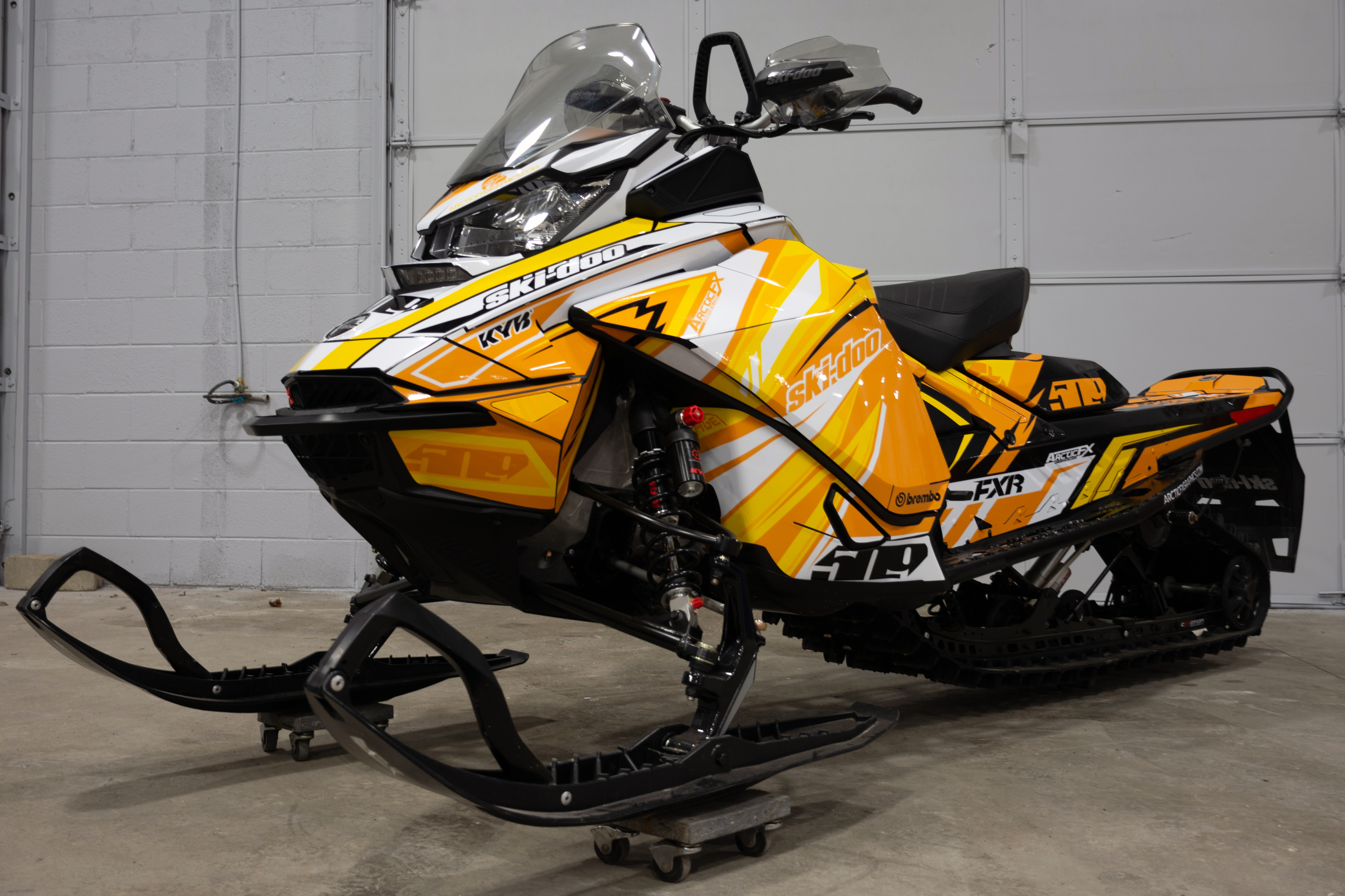 A Ski-Doo Gen4 Narrow Body snowmobile with a orange, white, and yellow Kesterke Adrenaline custom vinyl wrap.
