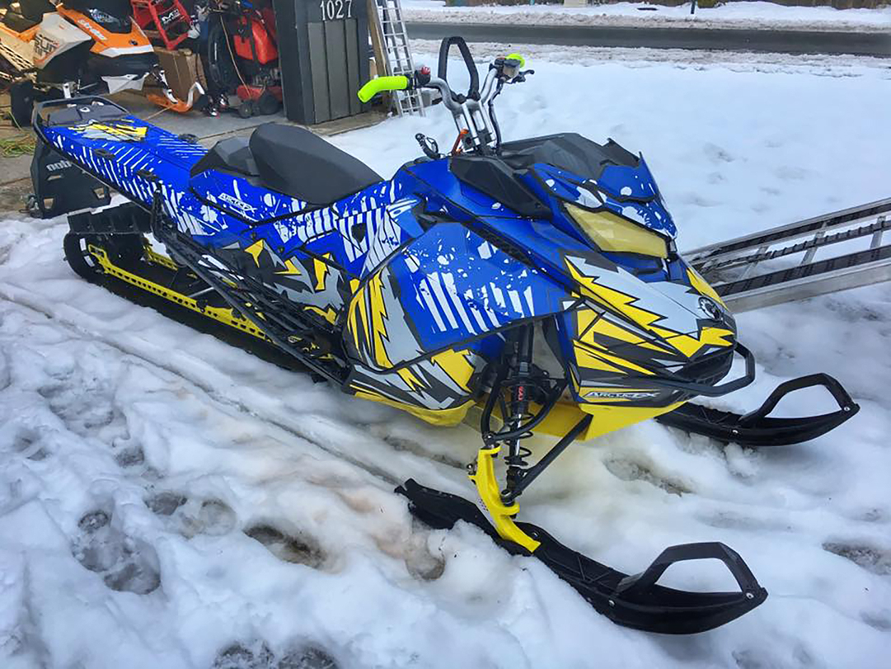 A Ski-Doo Gen4 Narrow Body snowmobile with a yellow, gray, and blue Altitude custom vinyl wrap.