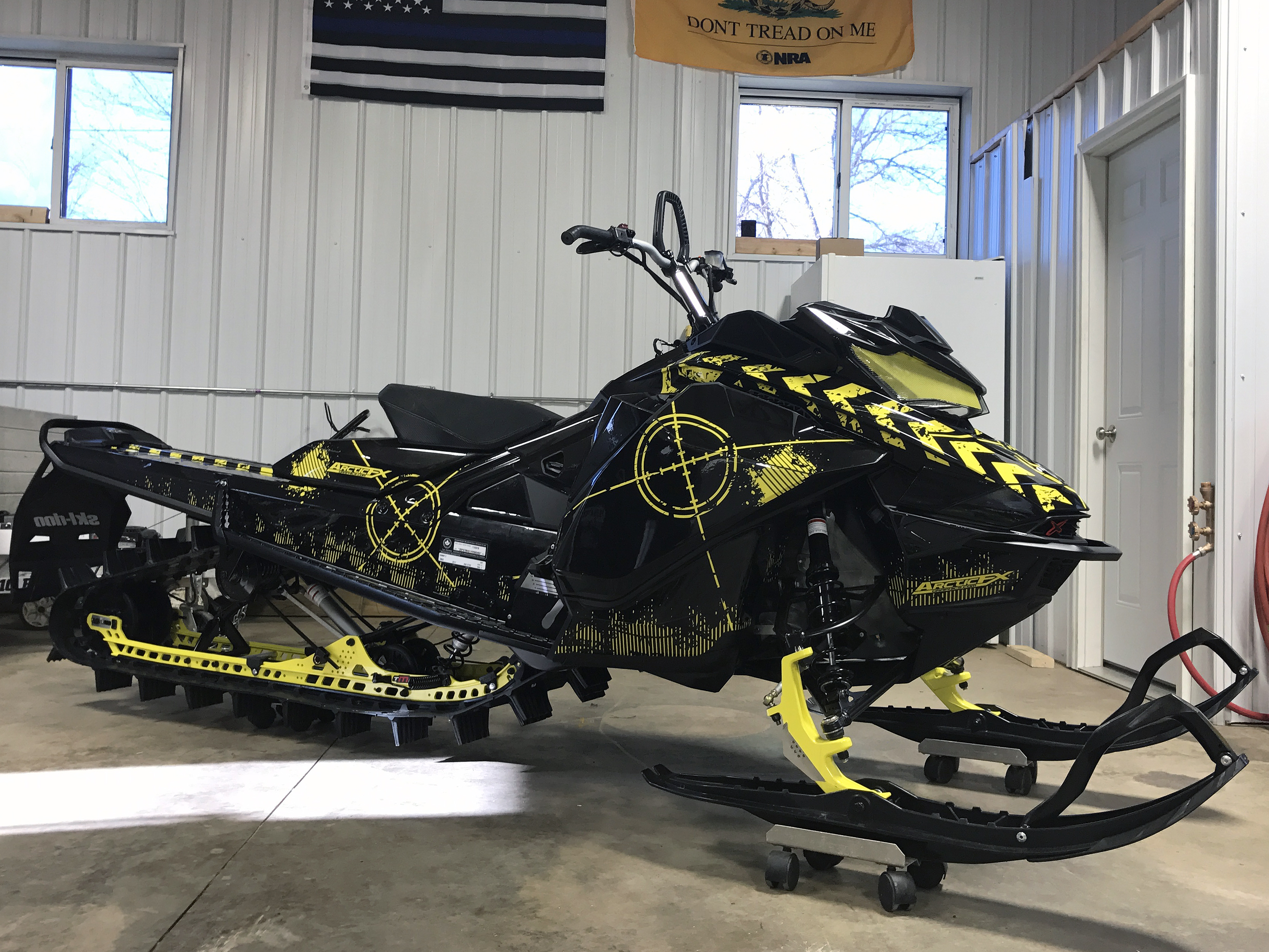 A Ski-Doo Gen4 Narrow Body snowmobile with a black and yellow Bombsquad custom vinyl wrap.