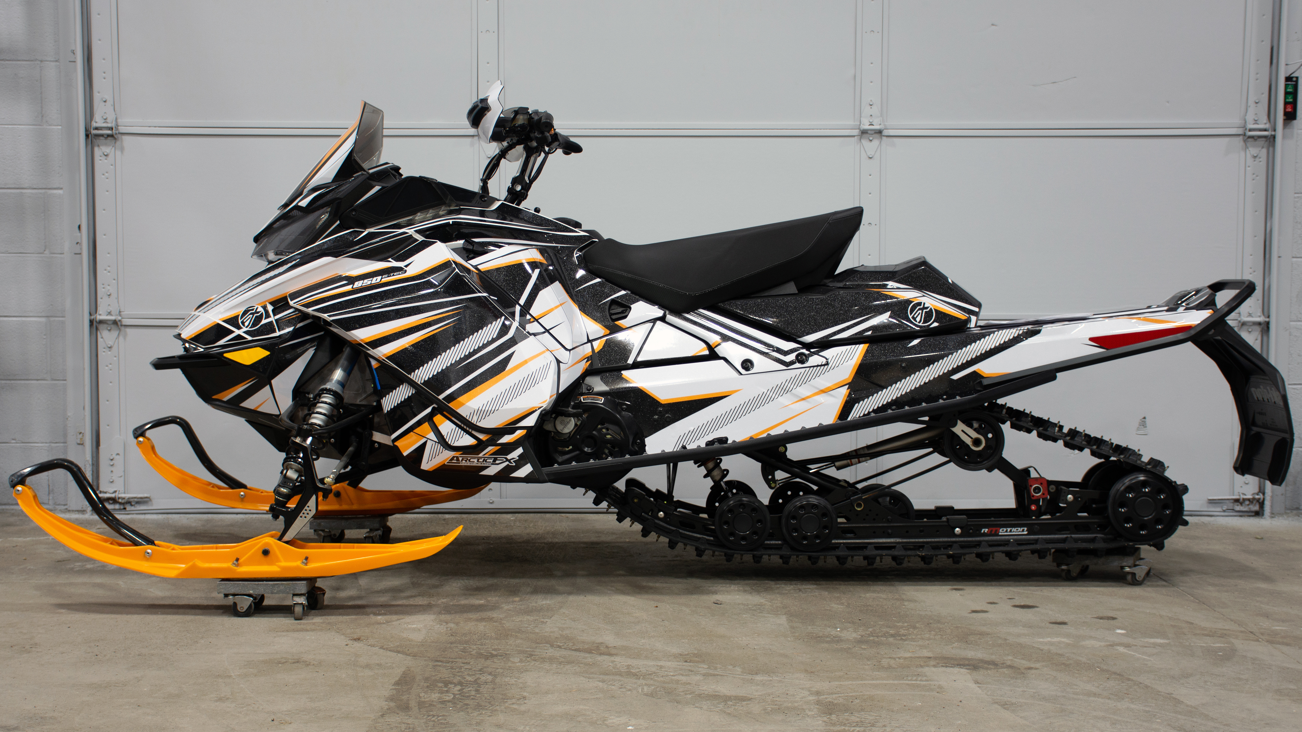A Ski-Doo Gen4 Narrow Body snowmobile with a orange, black, and white Bred2Win custom vinyl wrap.