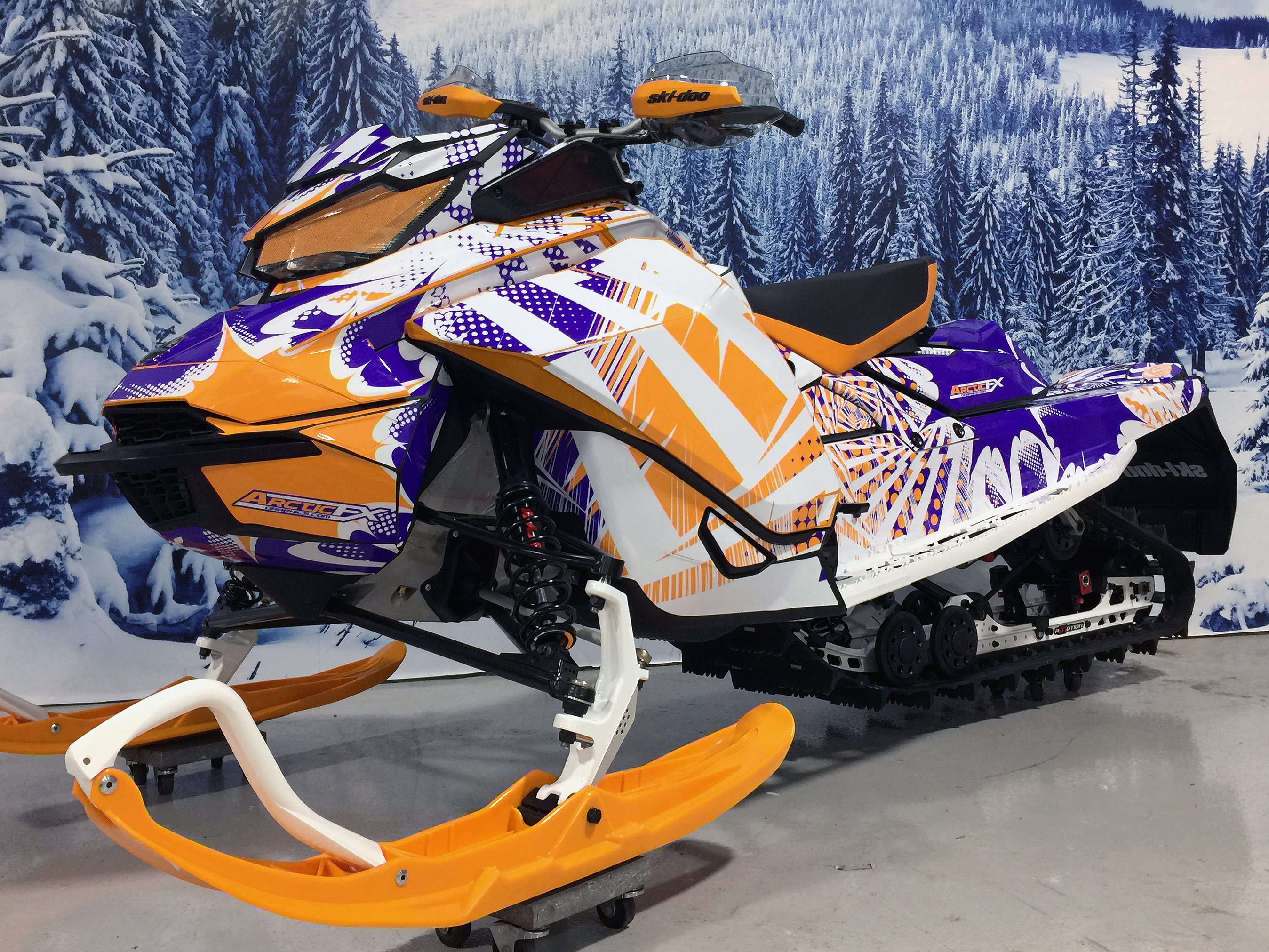 A Ski-Doo Gen4 Narrow Body snowmobile with a purple, white, and orange Delirious custom vinyl wrap.