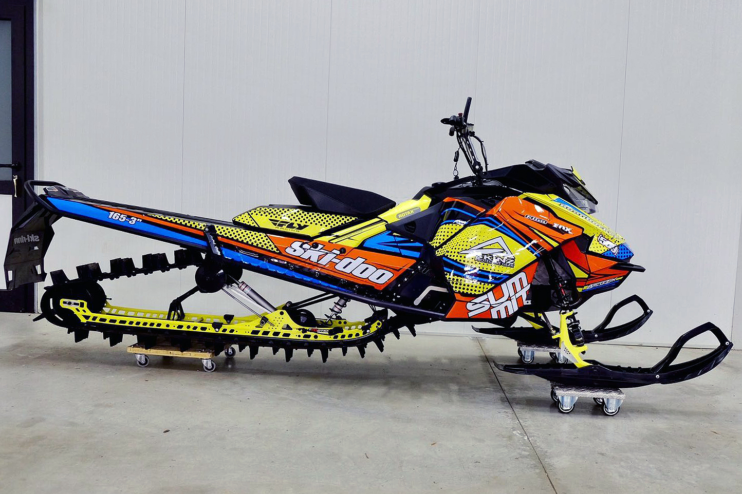 A Ski-Doo Gen4 Narrow Body snowmobile with a yellow, orange, and blue Halftone and Lines custom vinyl wrap.