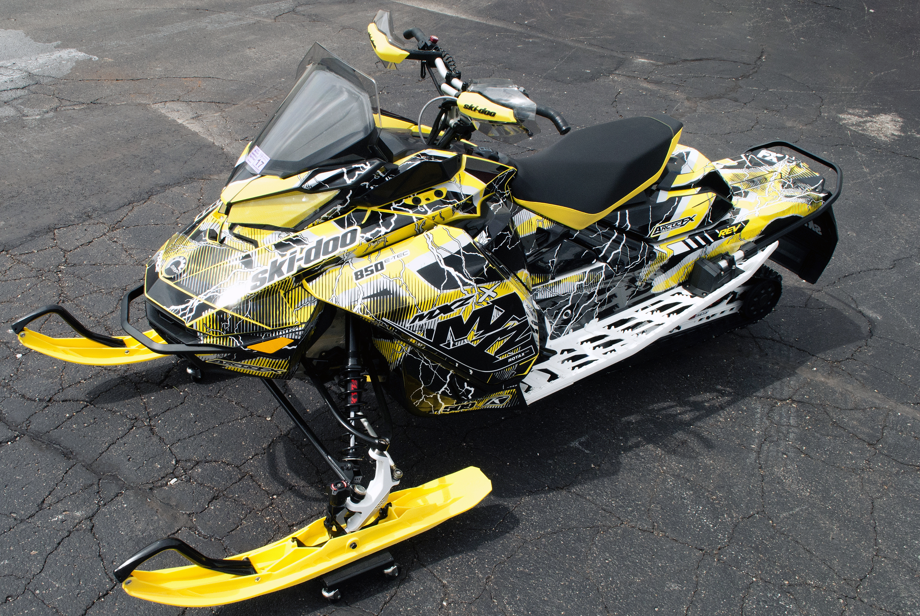 A Ski-Doo Gen4 Narrow Body snowmobile with a black, white, and yellow Hard Rain custom vinyl wrap.