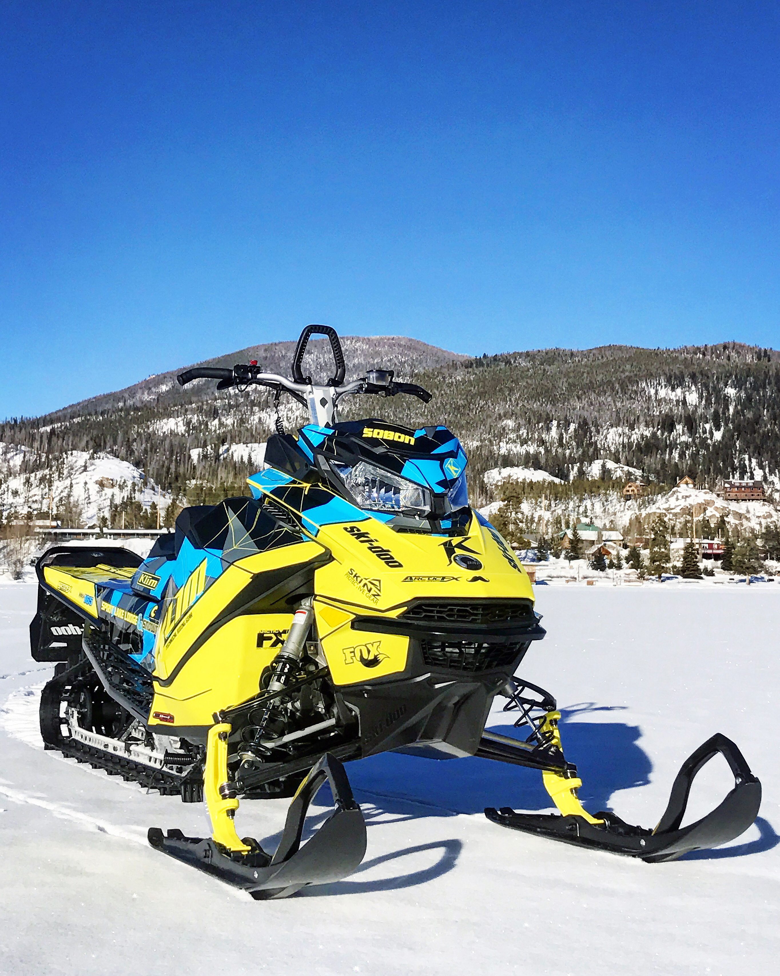 A Ski-Doo Gen4 Narrow Body snowmobile with a lime squeeze, blue, and gray Klim F3 Camo custom vinyl wrap.