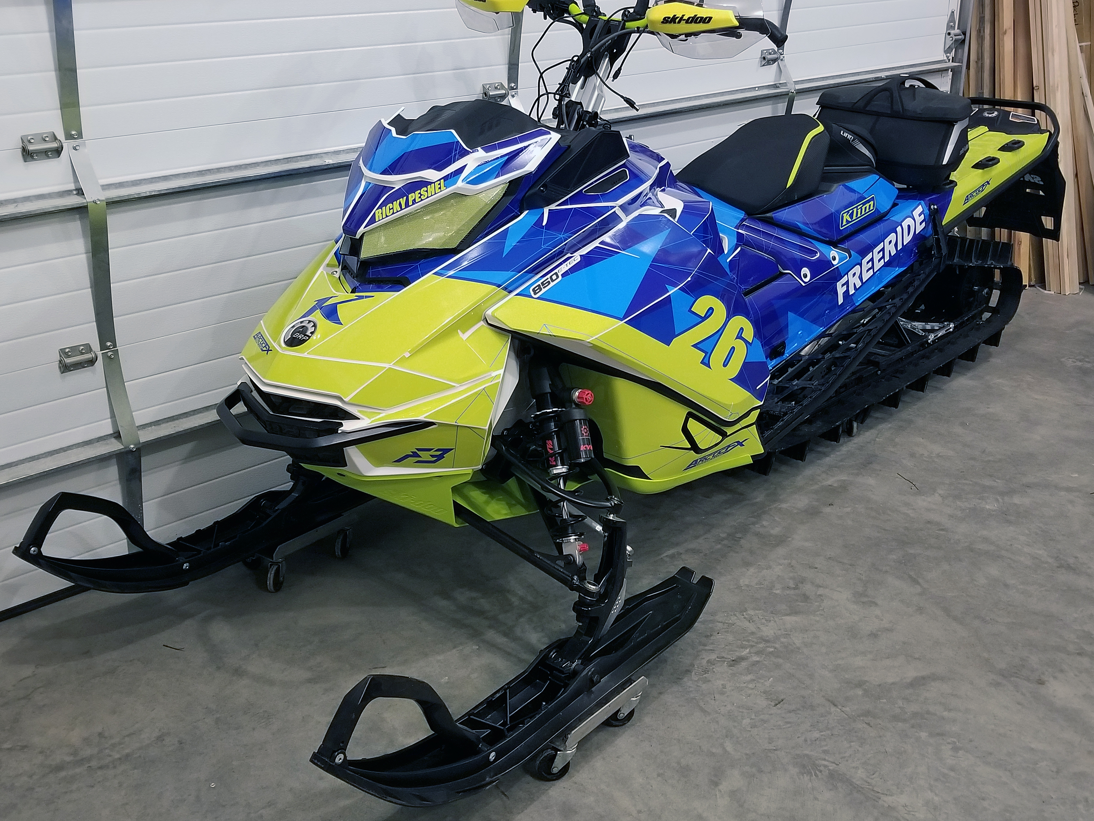 A Ski-Doo Gen4 Narrow Body snowmobile with a lime squeeze, blue, and white Klim F3 Camo custom vinyl wrap.