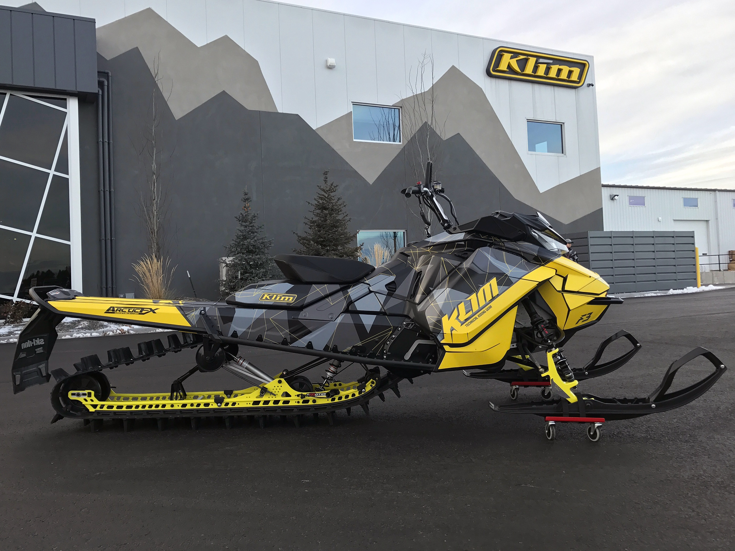 A Ski-Doo Gen4 Narrow Body snowmobile with a yellow, gray, and black Klim F3 Camo custom vinyl wrap.