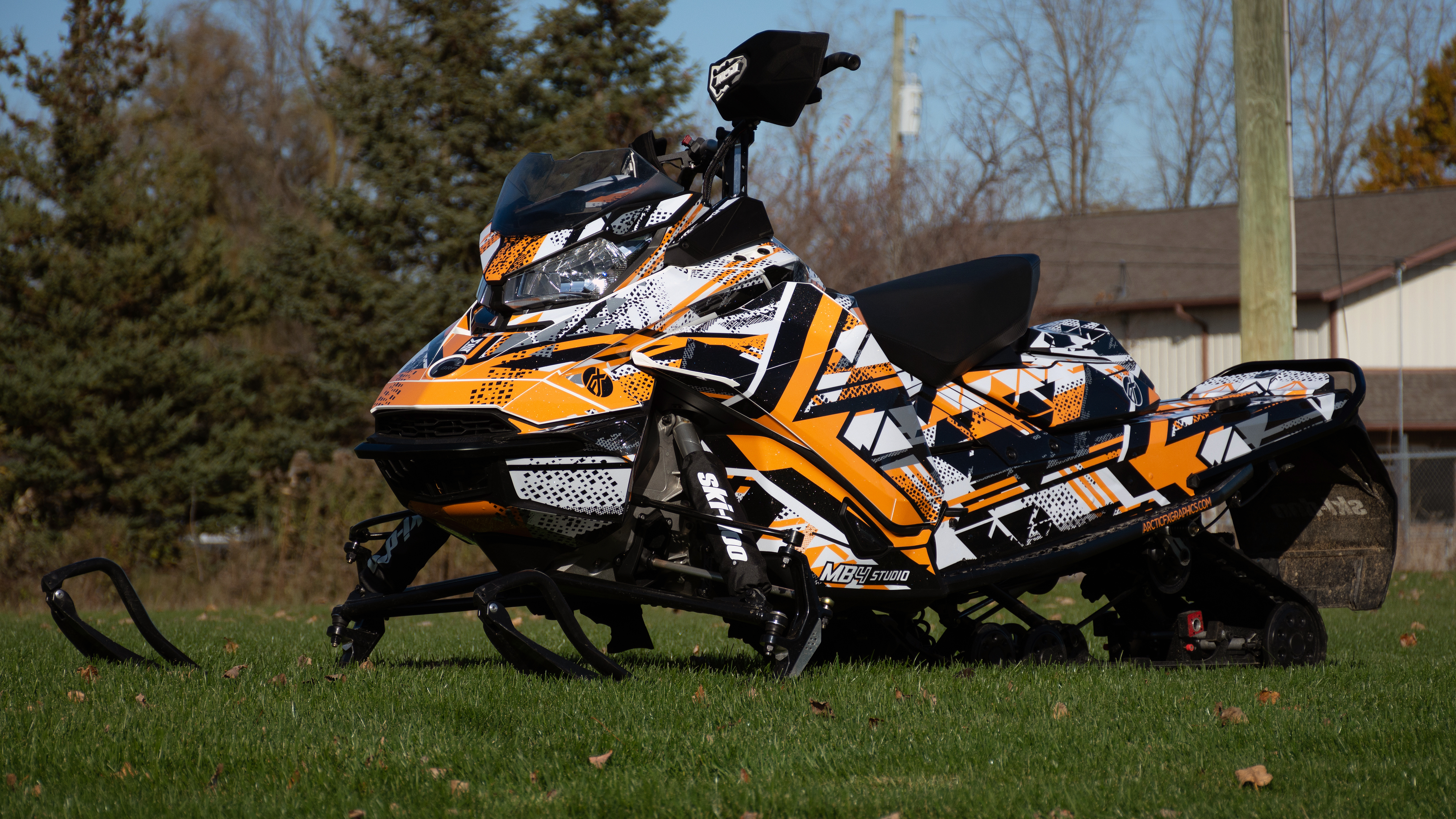 A Ski-Doo Gen4 Narrow Body snowmobile with a black, orange, and white MB4 Trifecta custom vinyl wrap.