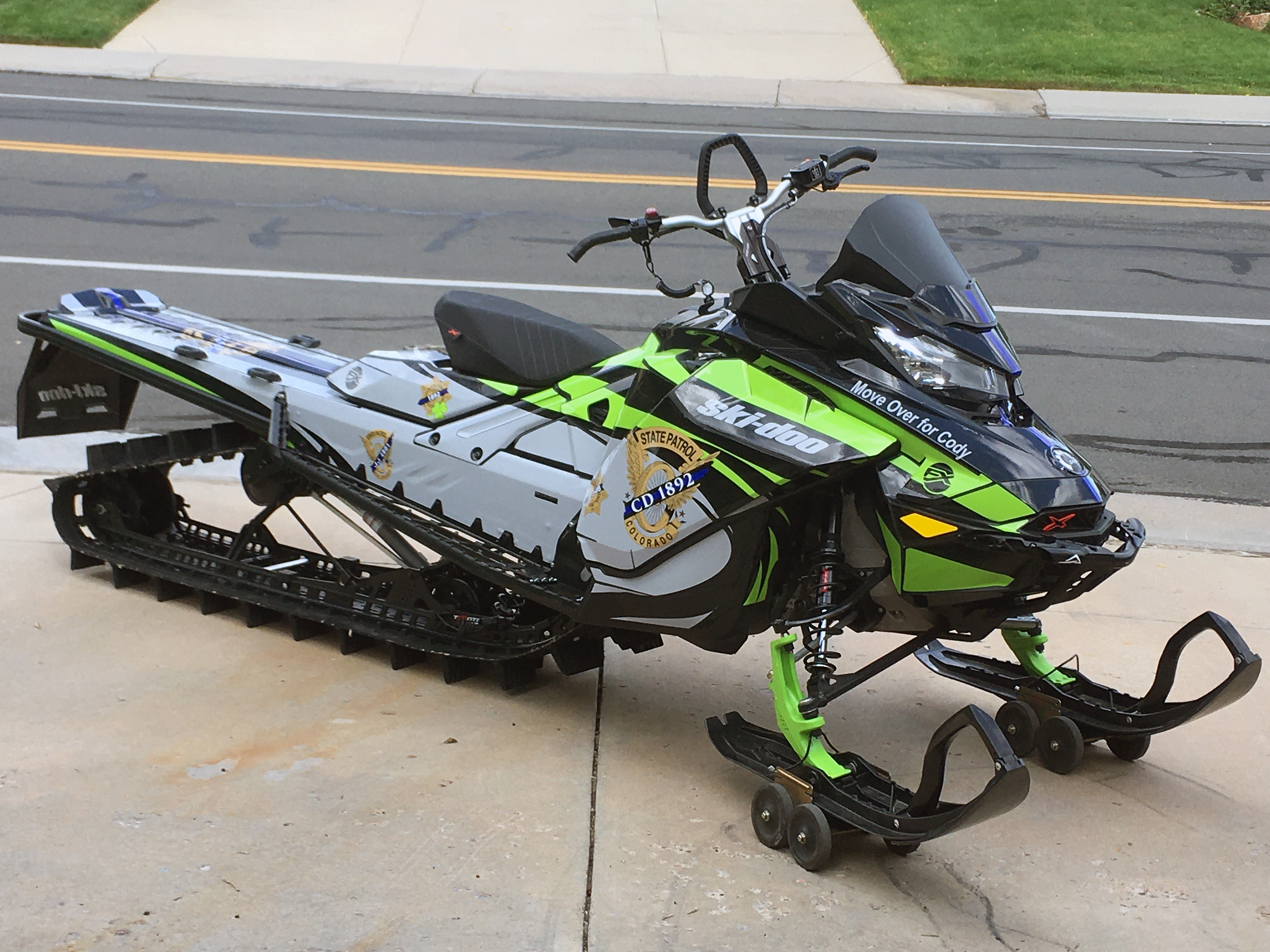 A Ski-Doo Gen4 Narrow Body snowmobile with a gray, green, and black State Trooper custom vinyl wrap.