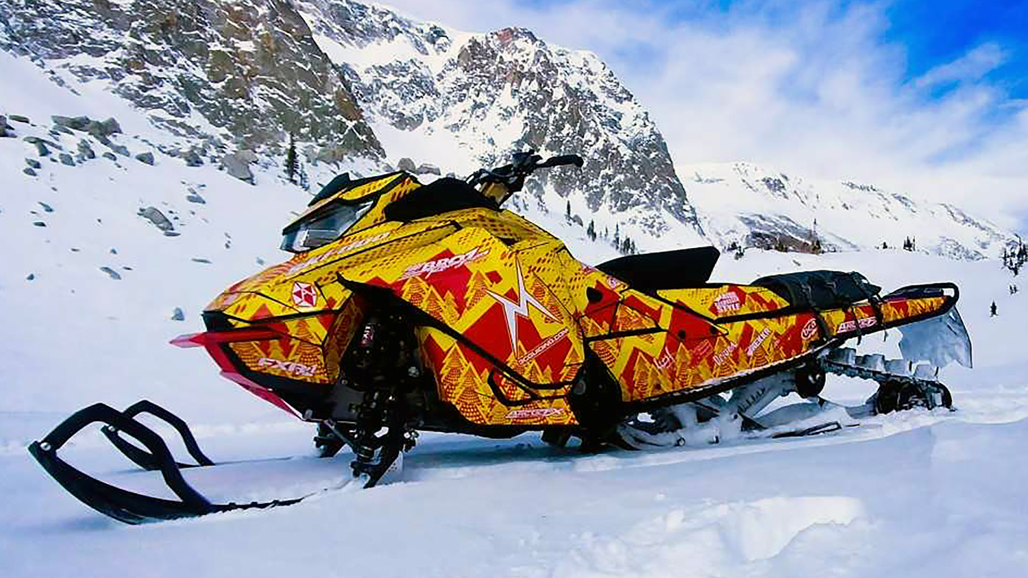 A Ski-Doo Gen4 Narrow Body snowmobile with a red, yellow, and white Vertex custom vinyl wrap.
