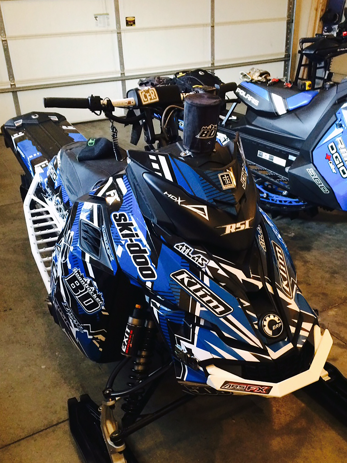 A Ski-Doo Rev XM snowmobile with a blue, white, and black Altitude City custom vinyl wrap.