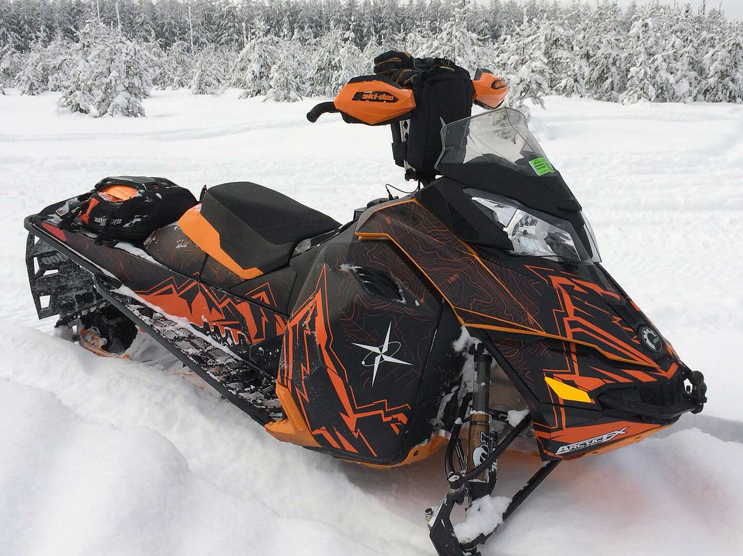 A Ski-Doo Rev XM snowmobile with a orange, and black Altitude Topo custom vinyl wrap.