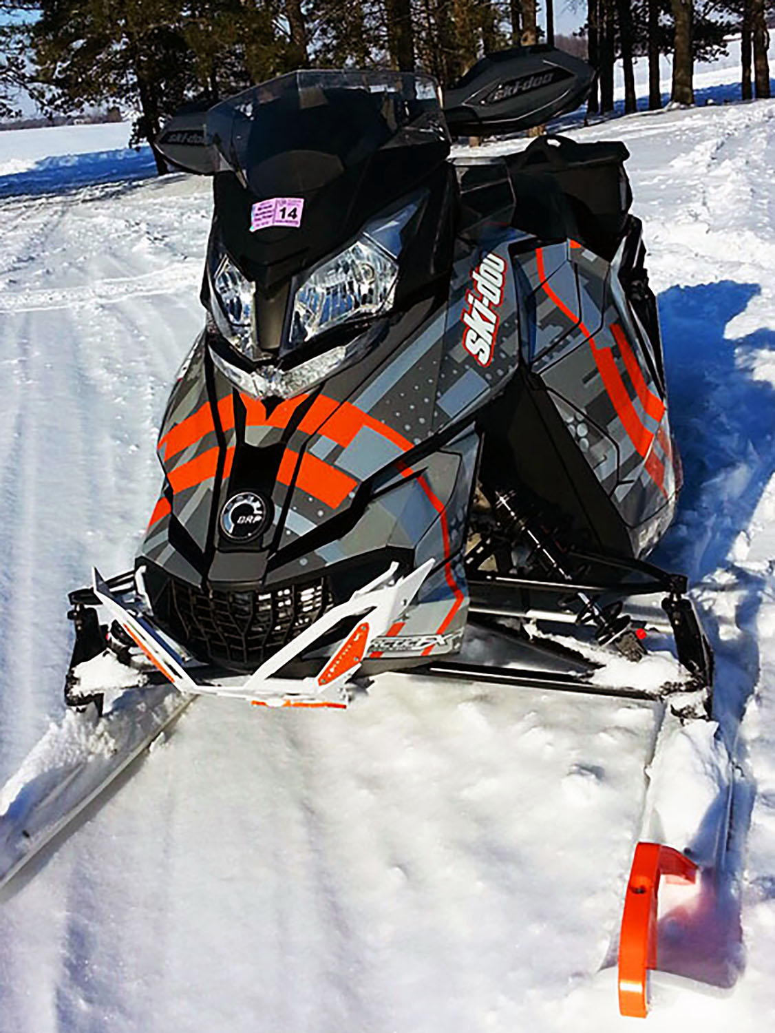 A Ski-Doo Rev XM snowmobile with a orange and gray Arc Reactor custom vinyl wrap.
