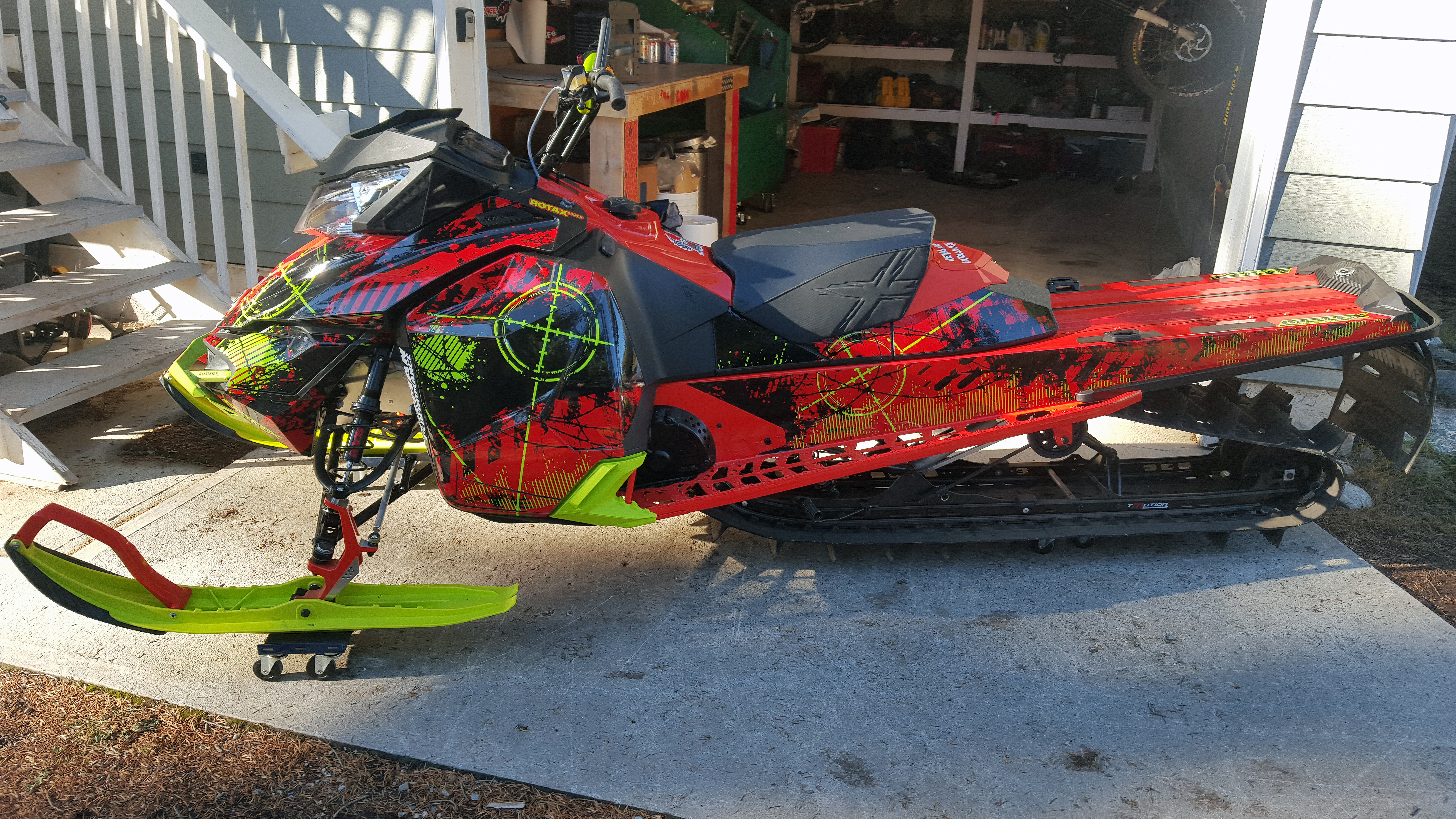 A Ski-Doo Rev XM snowmobile with a red, manta, and black Bombsquad custom vinyl wrap.