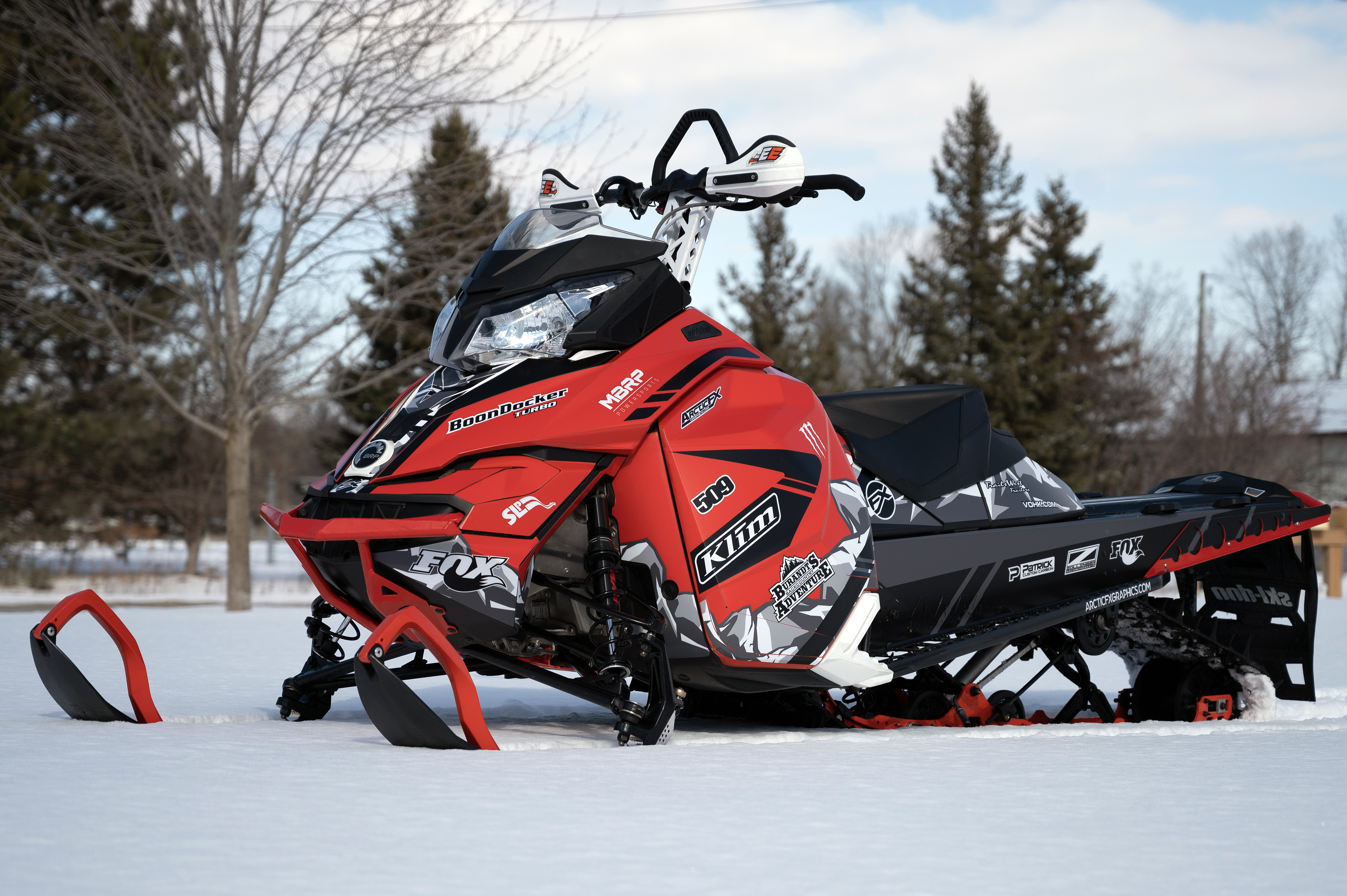 A Ski-Doo Rev XM snowmobile with a red, white, and black Burandt Vista custom vinyl wrap.