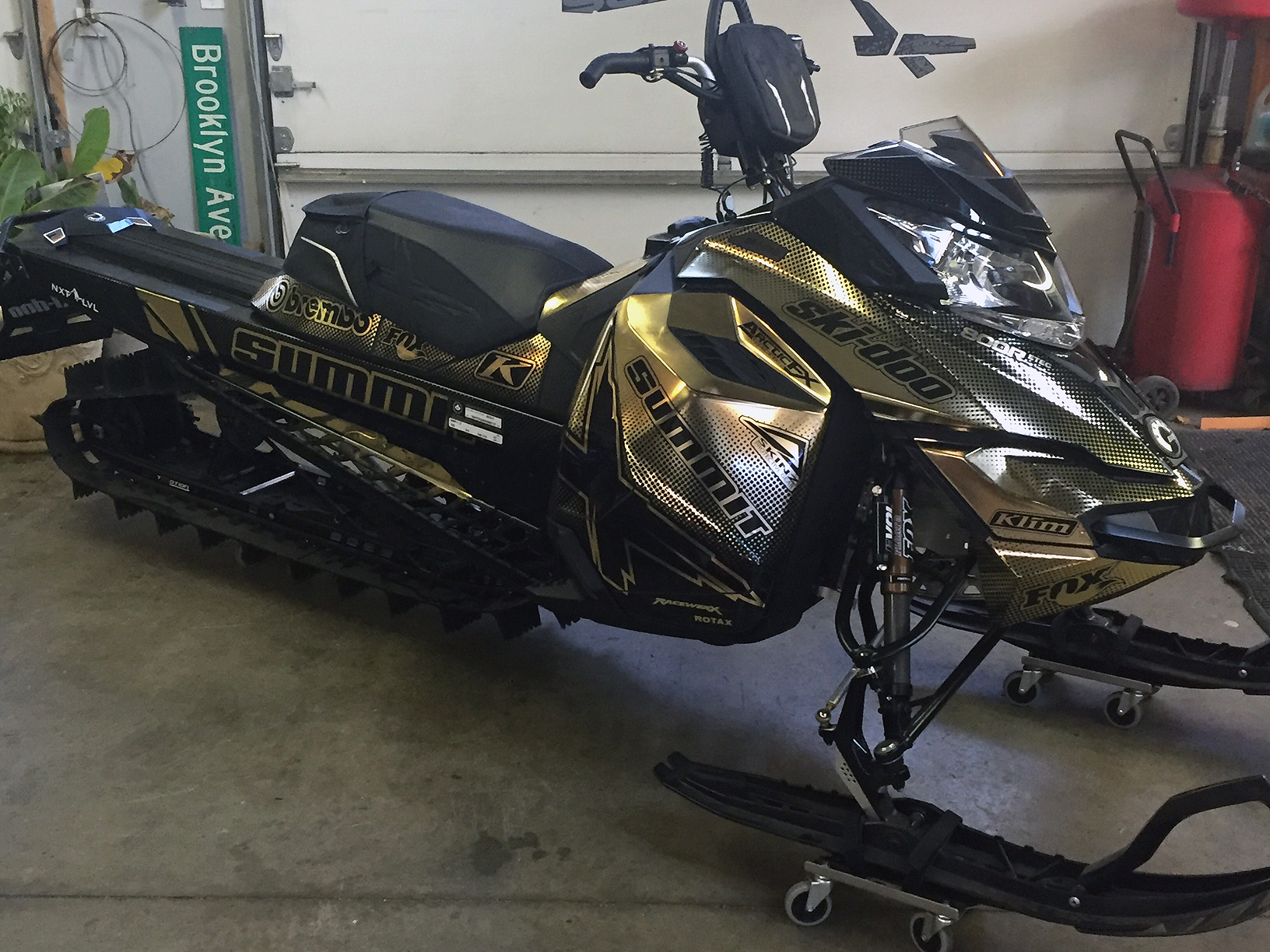 A Ski-Doo Rev XM snowmobile with a chrome, gold, and black Ellis custom vinyl wrap.