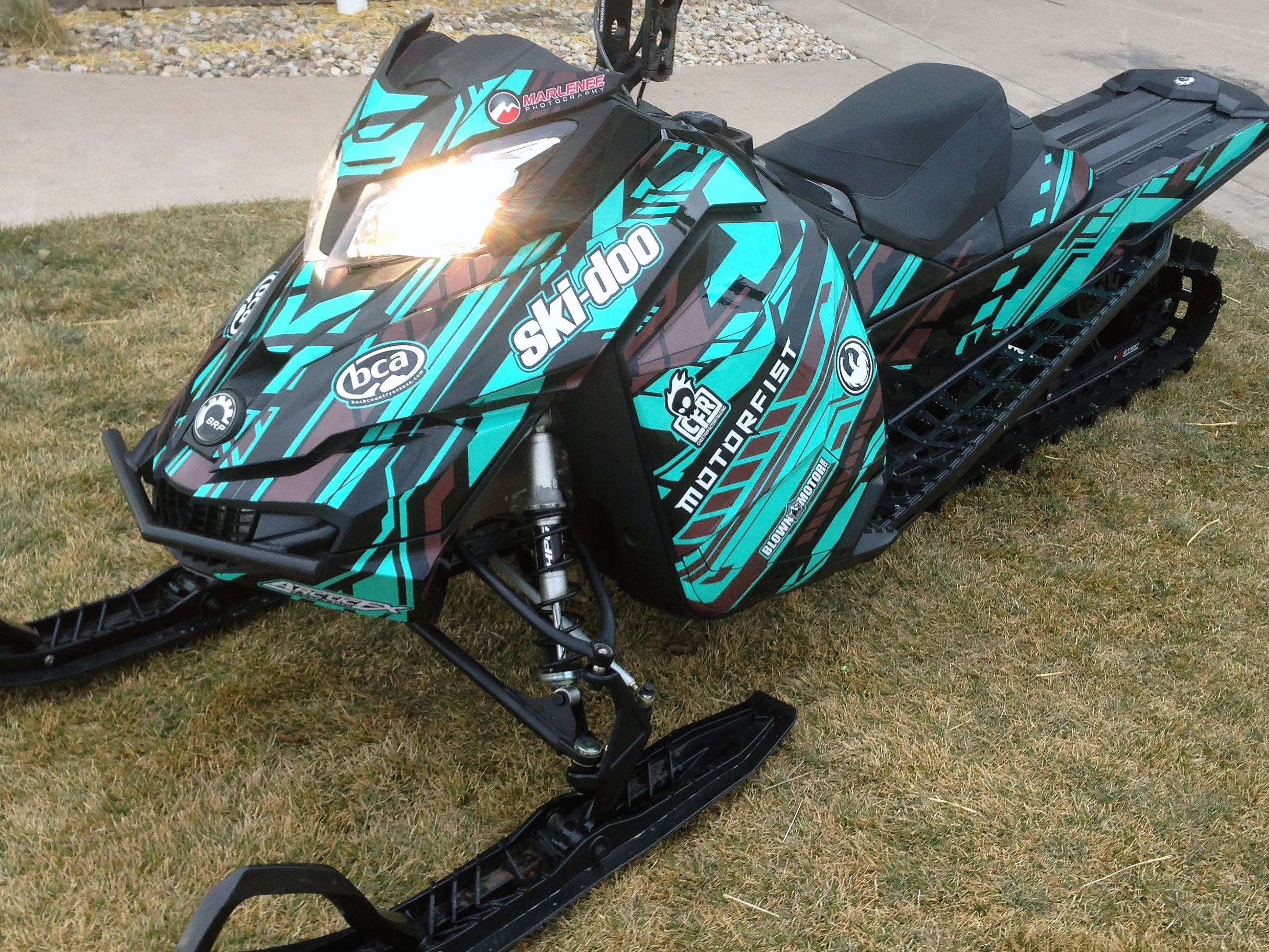 A Ski-Doo Rev XM snowmobile with a aqua, brown, and black Evasion custom vinyl wrap.