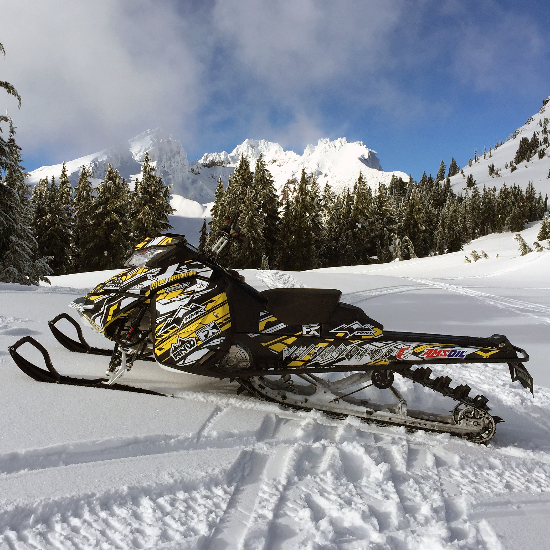 A Ski-Doo Rev XM snowmobile with a yellow, white, and black Evasion custom vinyl wrap.