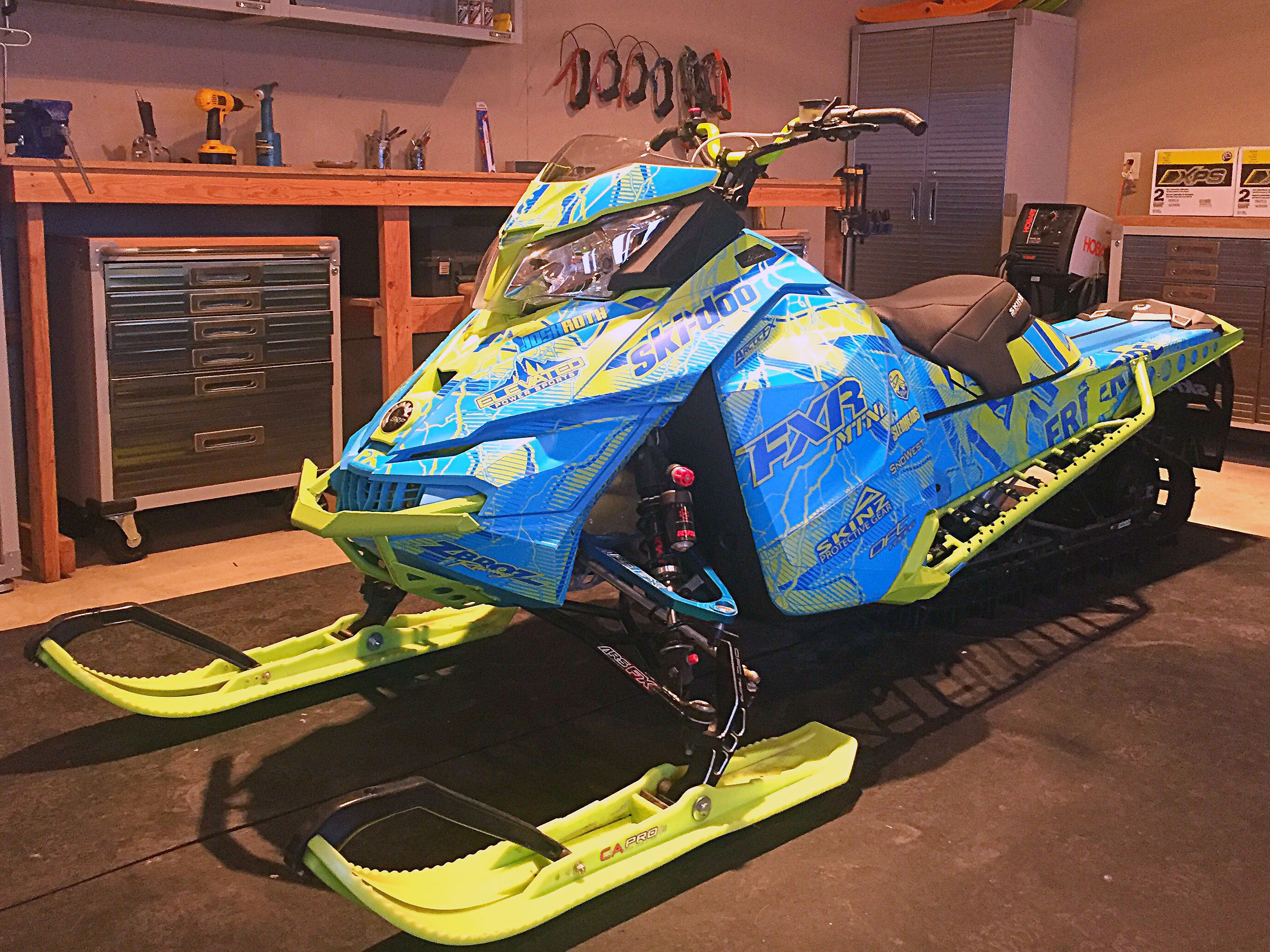 A Ski-Doo Rev XM snowmobile with a octane blue, manta, and blue Hard Rain custom vinyl wrap.