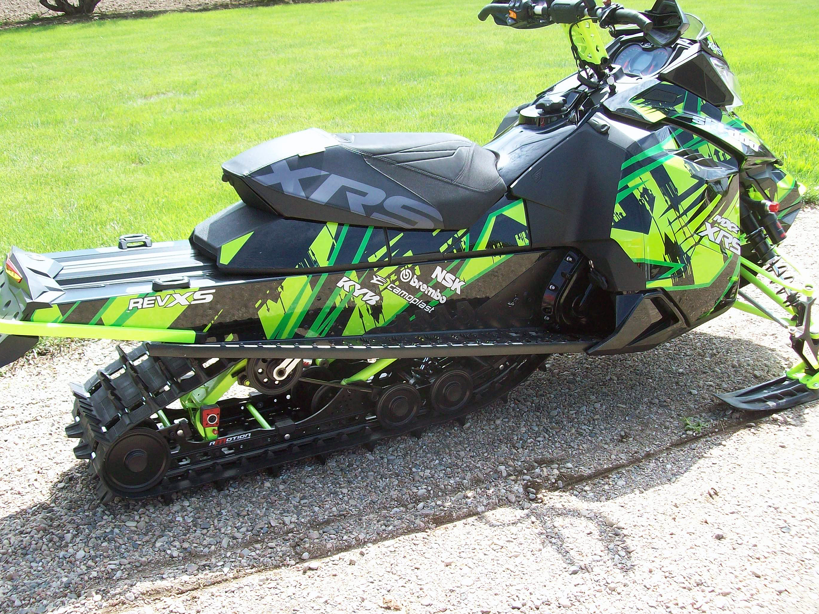 A Ski-Doo Rev XM snowmobile with a green, manta, and black Insidious custom vinyl wrap.