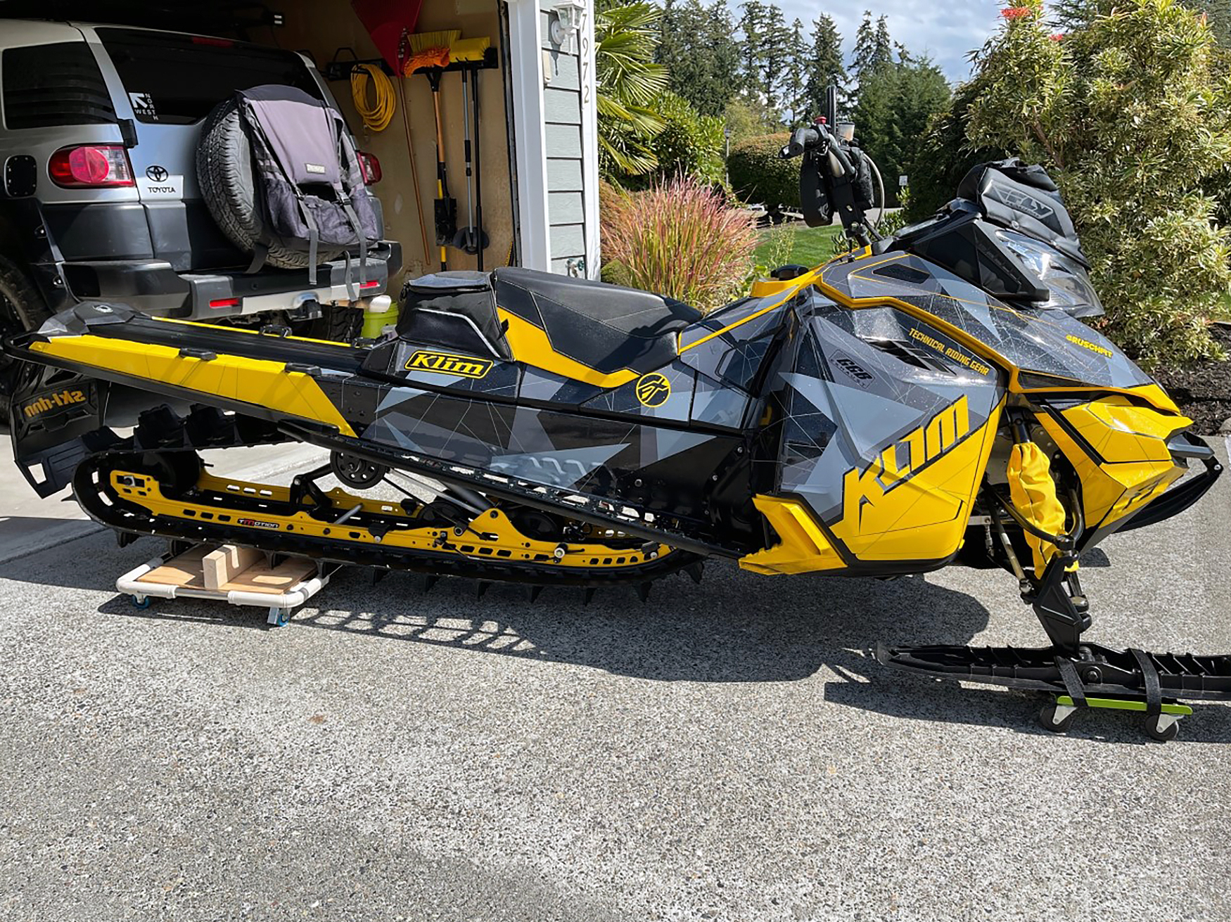 A Ski-Doo Rev XM snowmobile with a gray, yellow, and black Klim F3 Camo custom vinyl wrap.