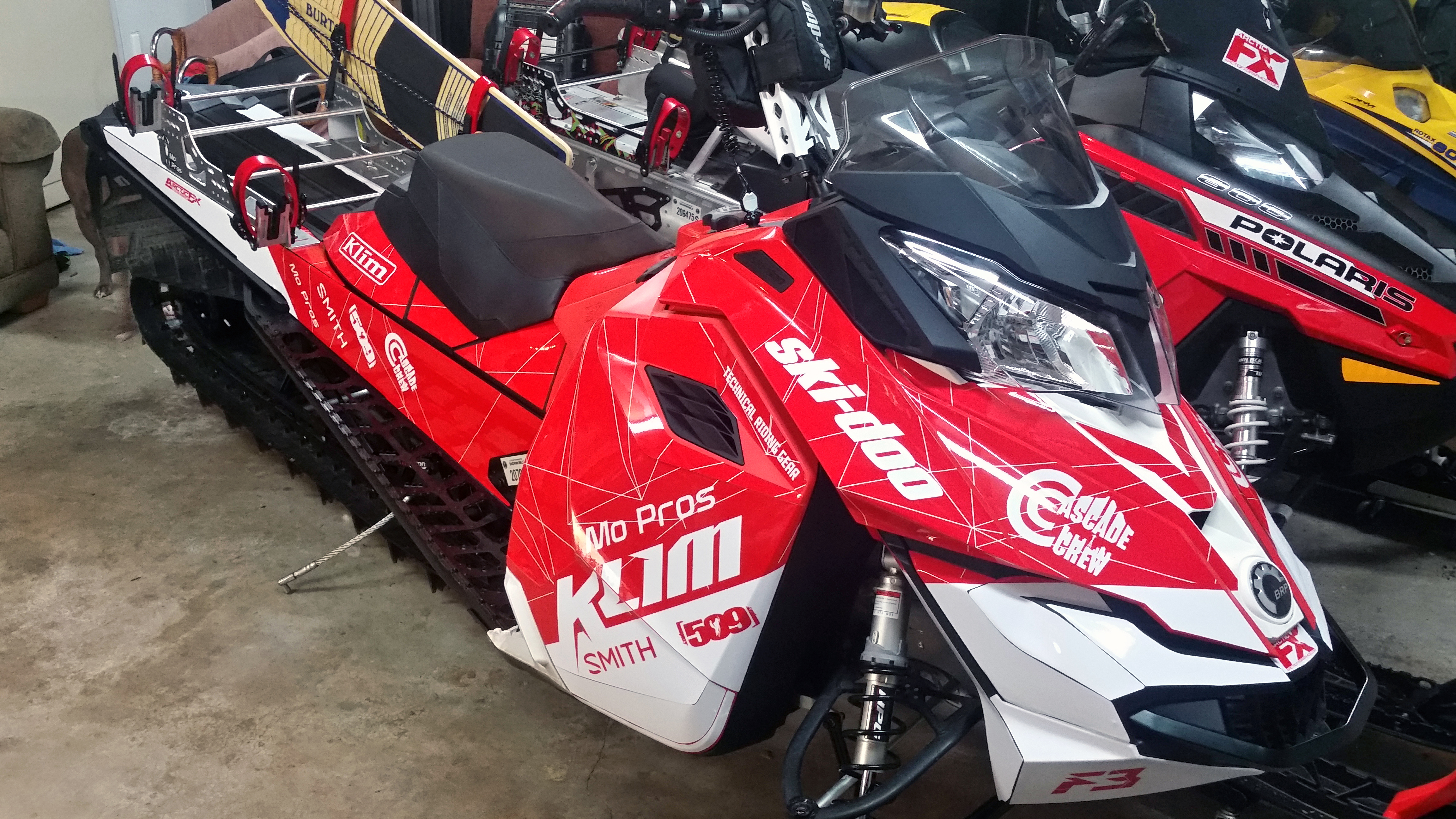 A Ski-Doo Rev XM snowmobile with a red and white Klim F3 Camo custom vinyl wrap.
