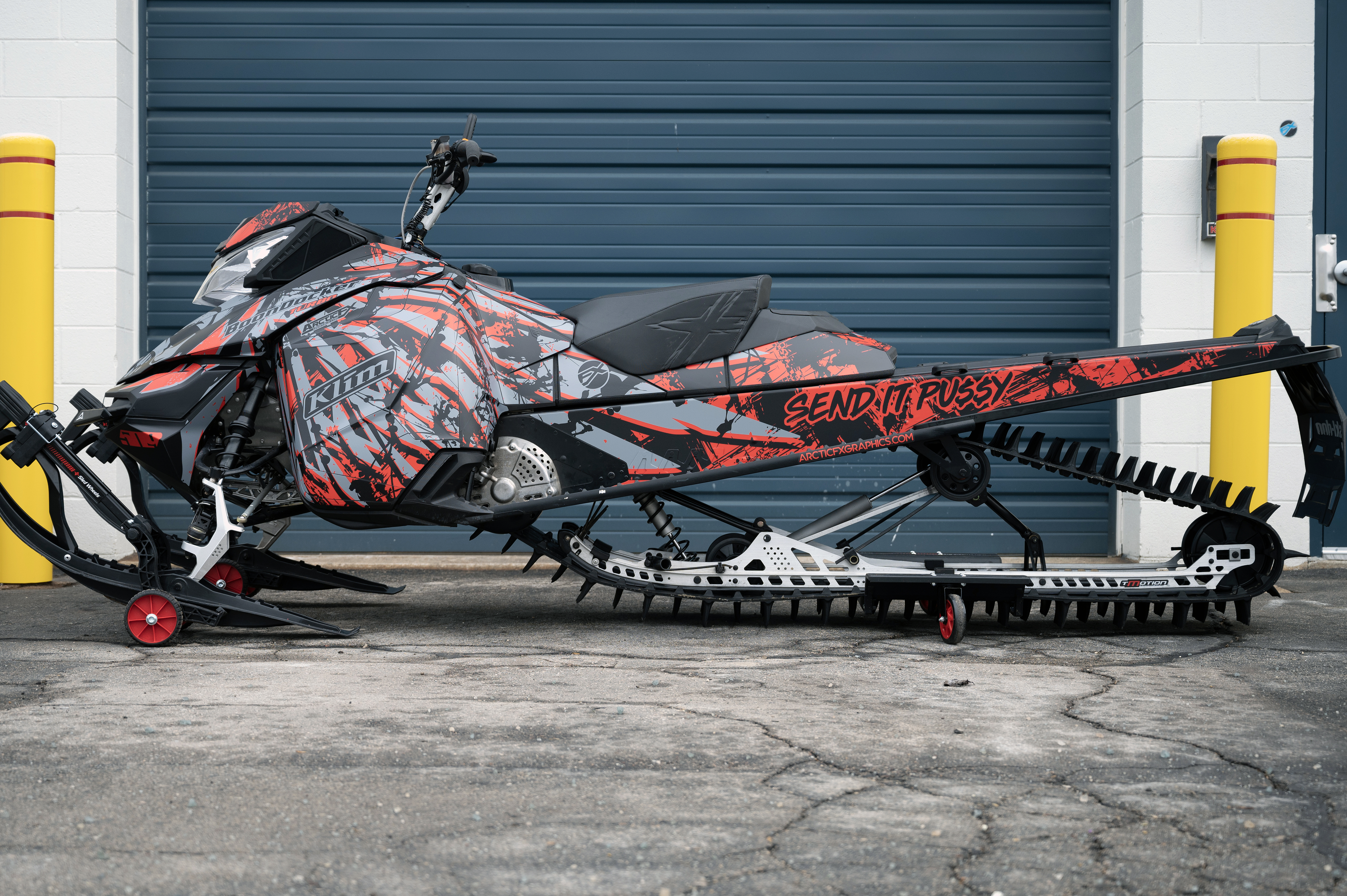 A Ski-Doo Rev XM snowmobile with a black, red, and gray Nemesis custom vinyl wrap.