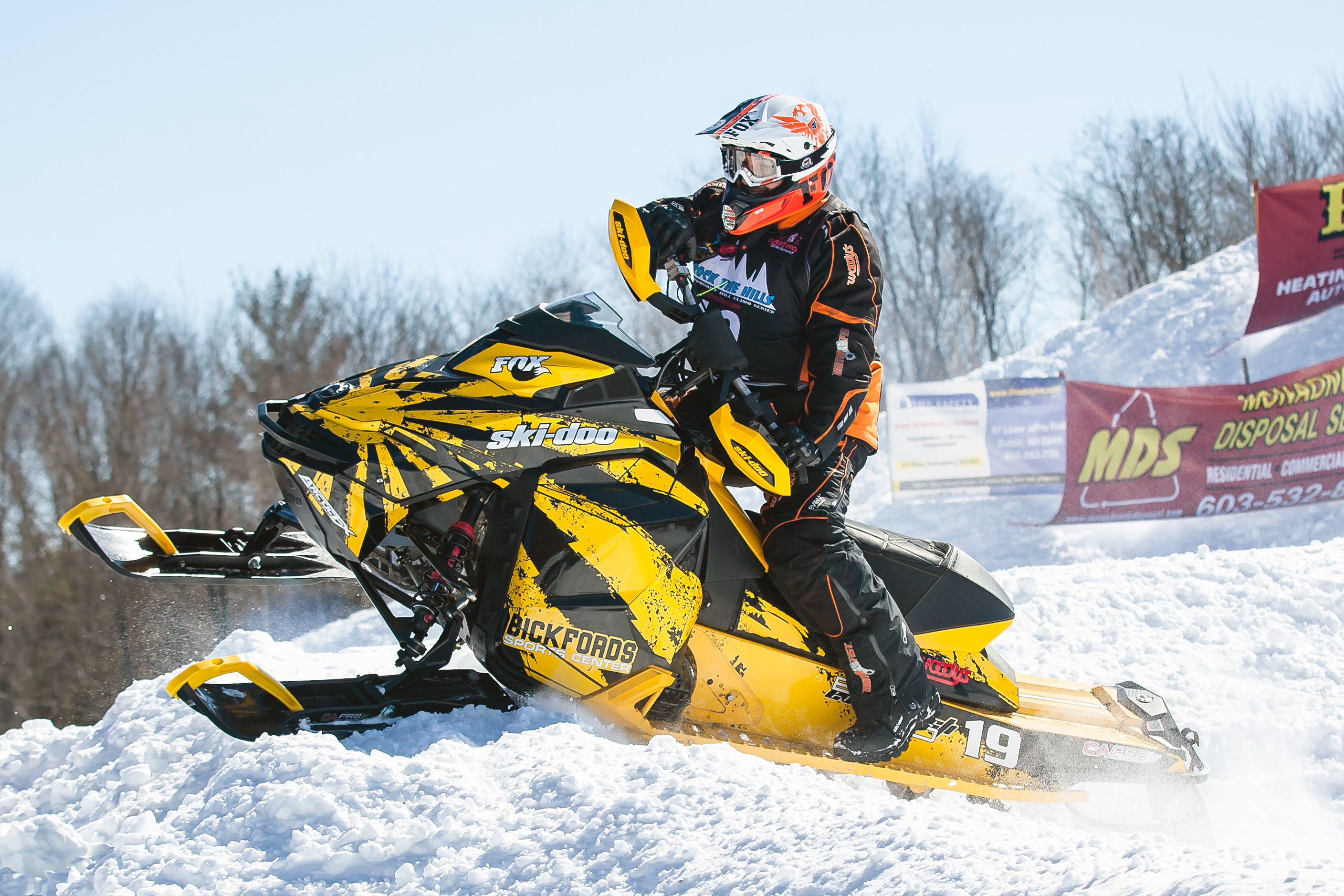 A Ski-Doo Rev XM snowmobile with a yellow and black Rising Sun custom vinyl wrap.