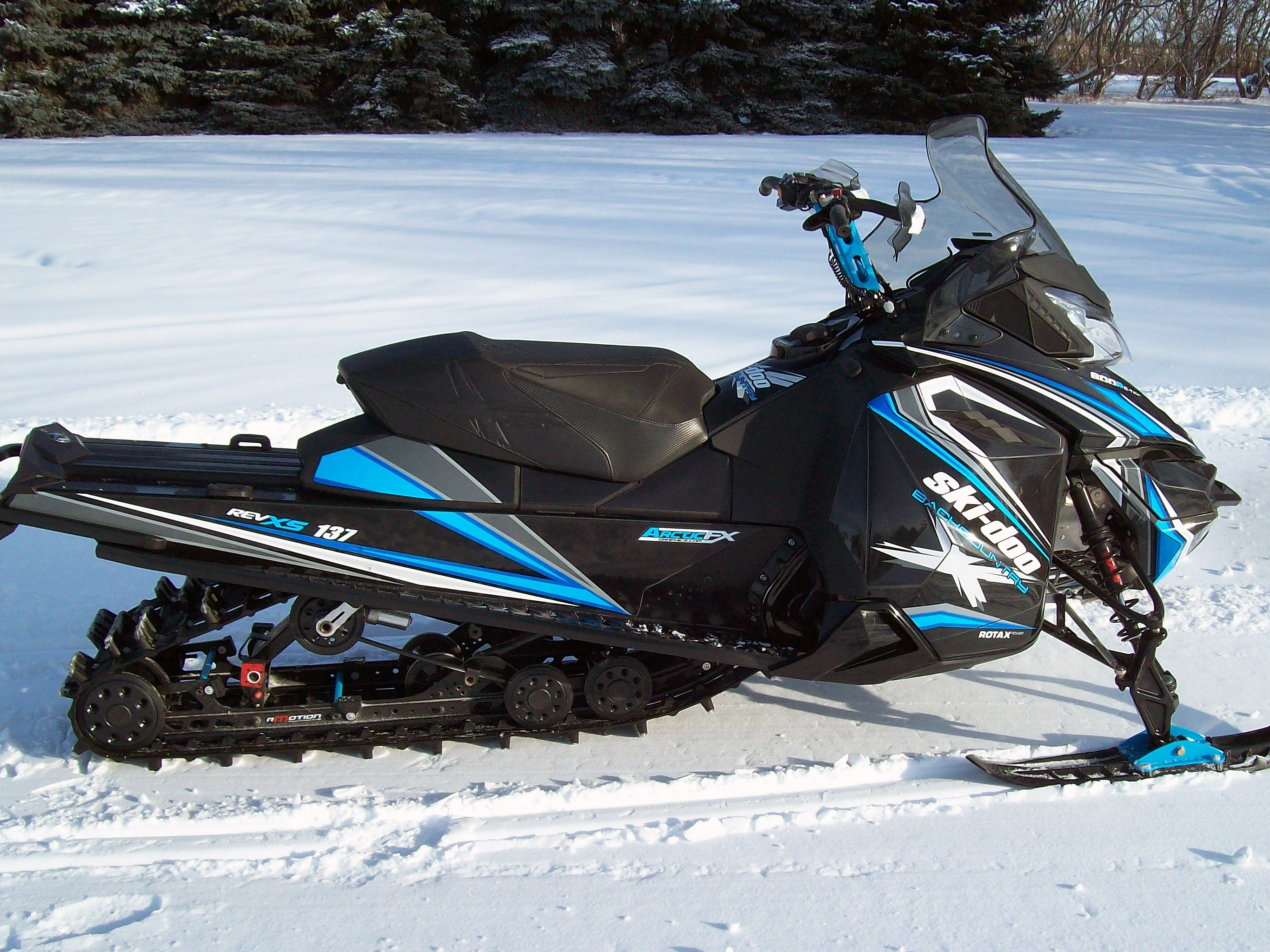A Ski-Doo Rev XM snowmobile with a blue, white, and black Robson custom vinyl wrap.