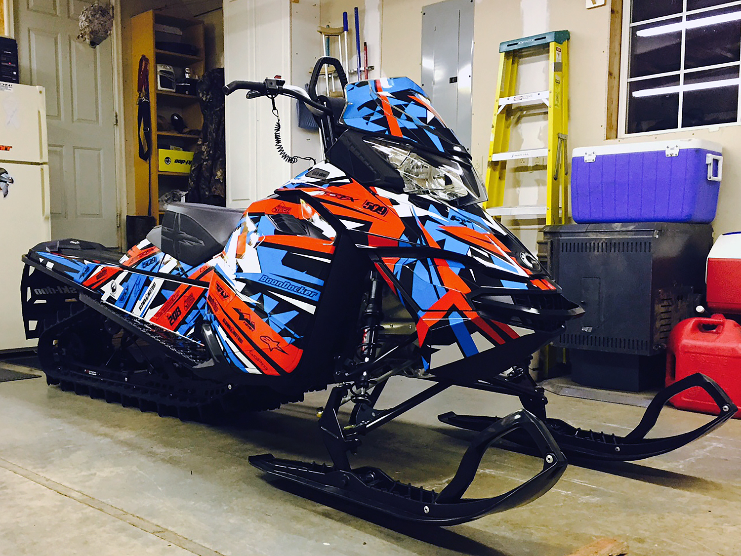 A Ski-Doo Rev XM snowmobile with a blue, white, red, and black Shattered custom vinyl wrap.