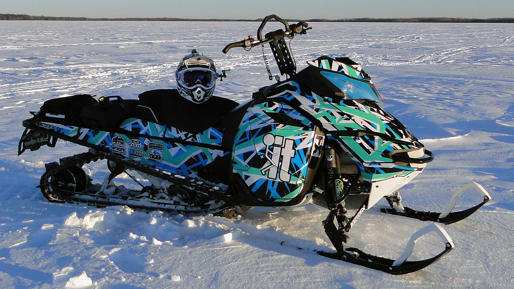 A Ski-Doo Rev XM snowmobile with a aqua, white, black, and blue Shattered Illusion custom vinyl wrap.