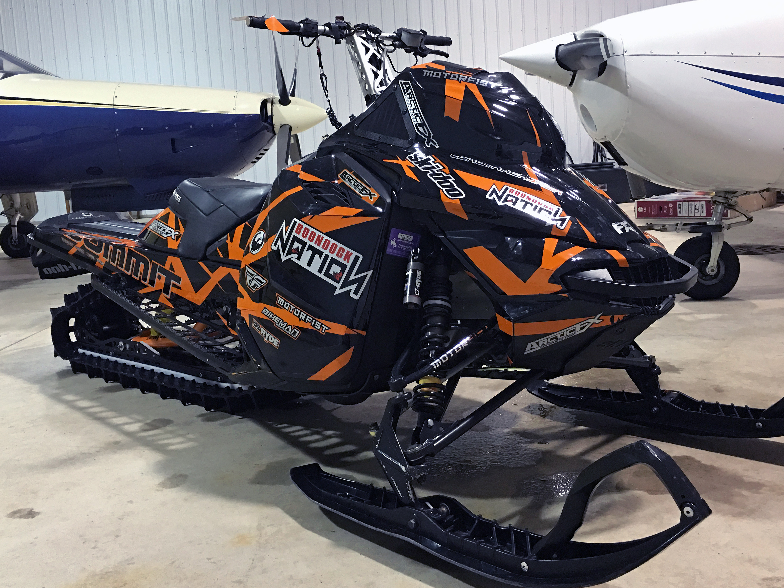 A Ski-Doo Rev XM snowmobile with a orange and black Shattered Illusion custom vinyl wrap.