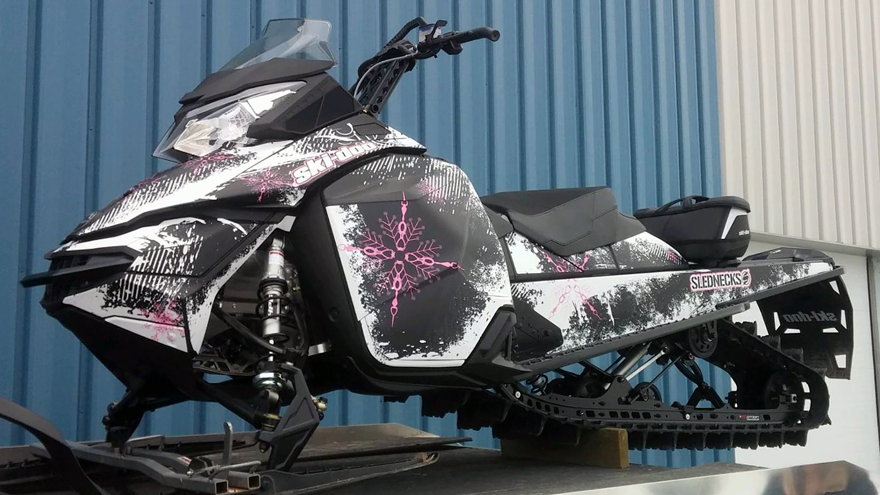 A Ski-Doo Rev XM snowmobile with a pink, white, and black Snow Storm custom vinyl wrap.
