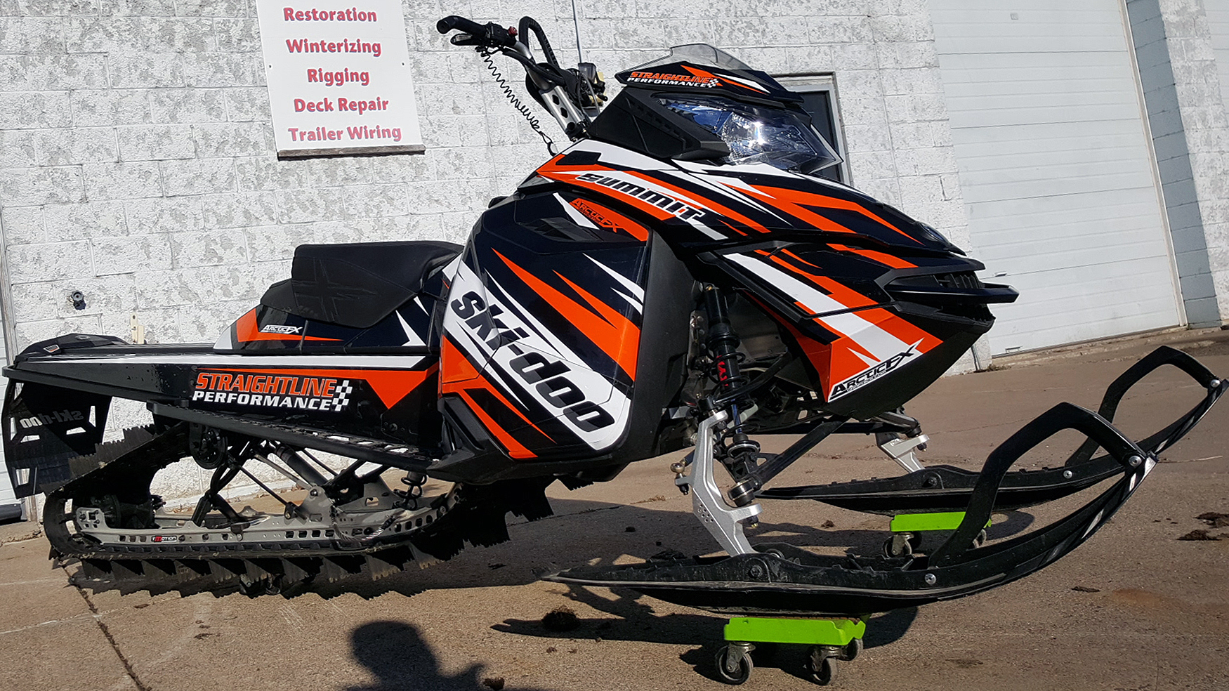 A Ski-Doo Rev XM snowmobile with a white, orange, and black StraightLine custom vinyl wrap.