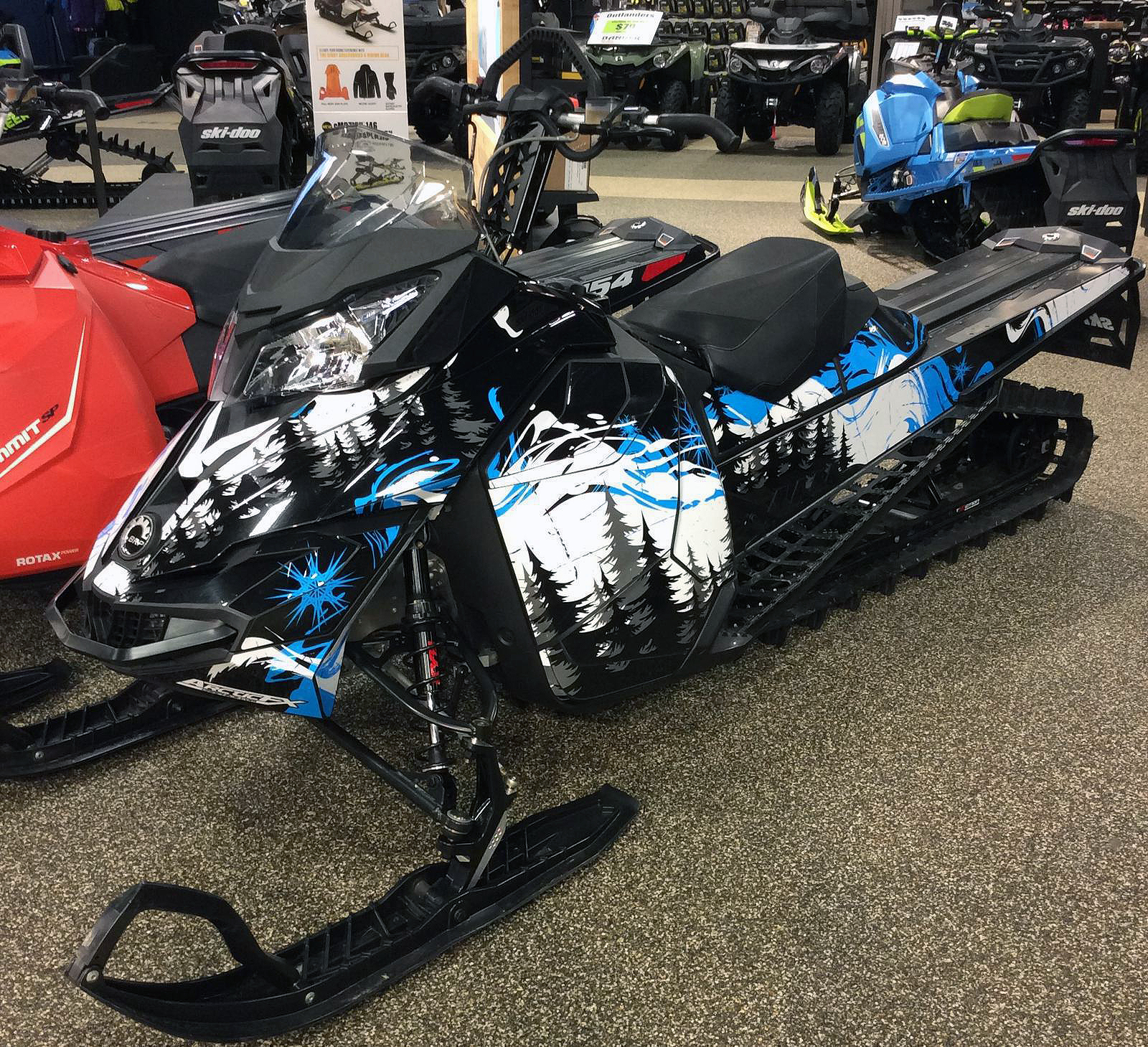 A Ski-Doo Rev XM snowmobile with a white, octane blue, and black Sub Zero custom vinyl wrap.