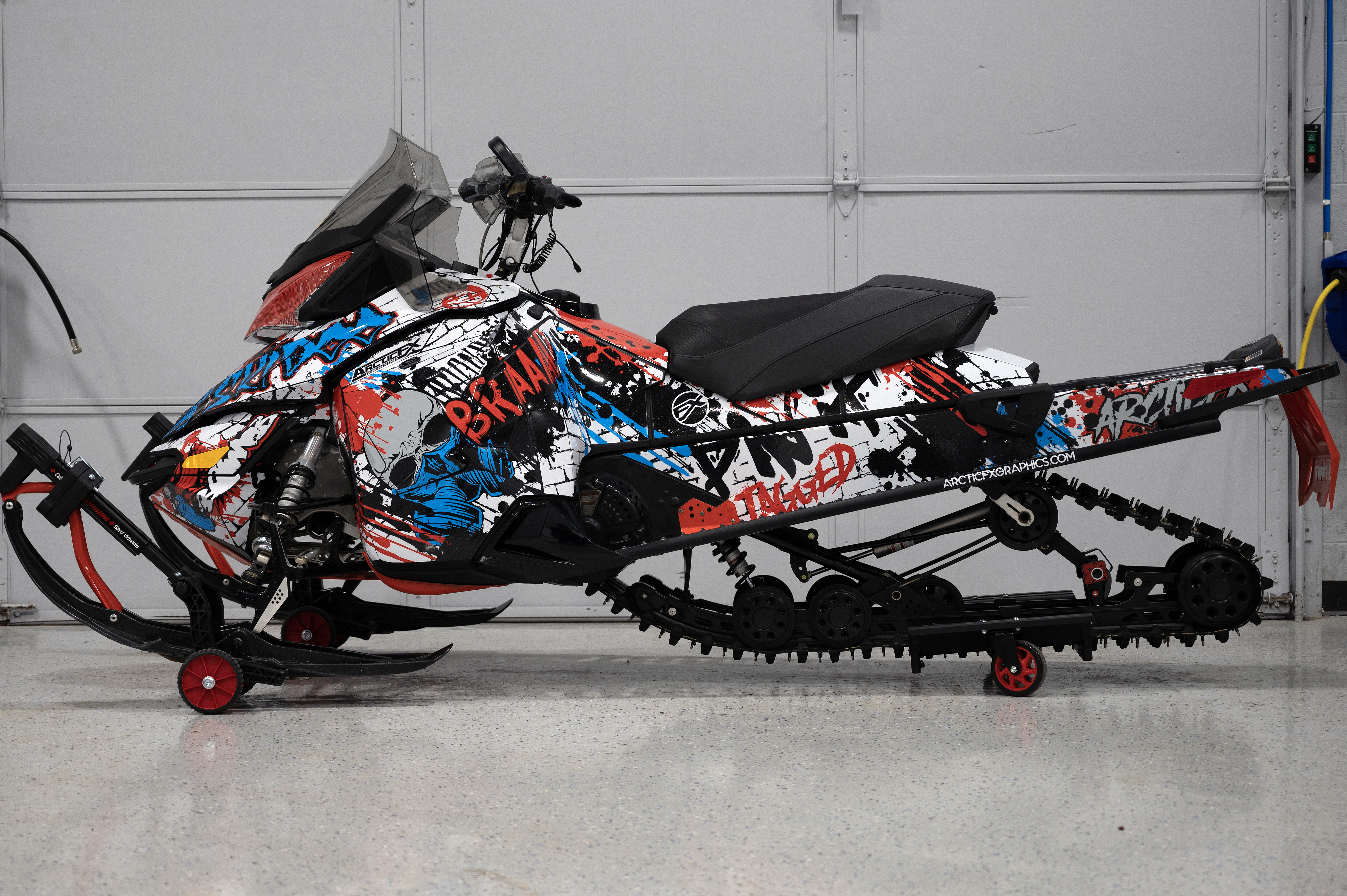 A Ski-Doo Rev XM snowmobile with a red, octane blue, and white Tagged custom vinyl wrap.