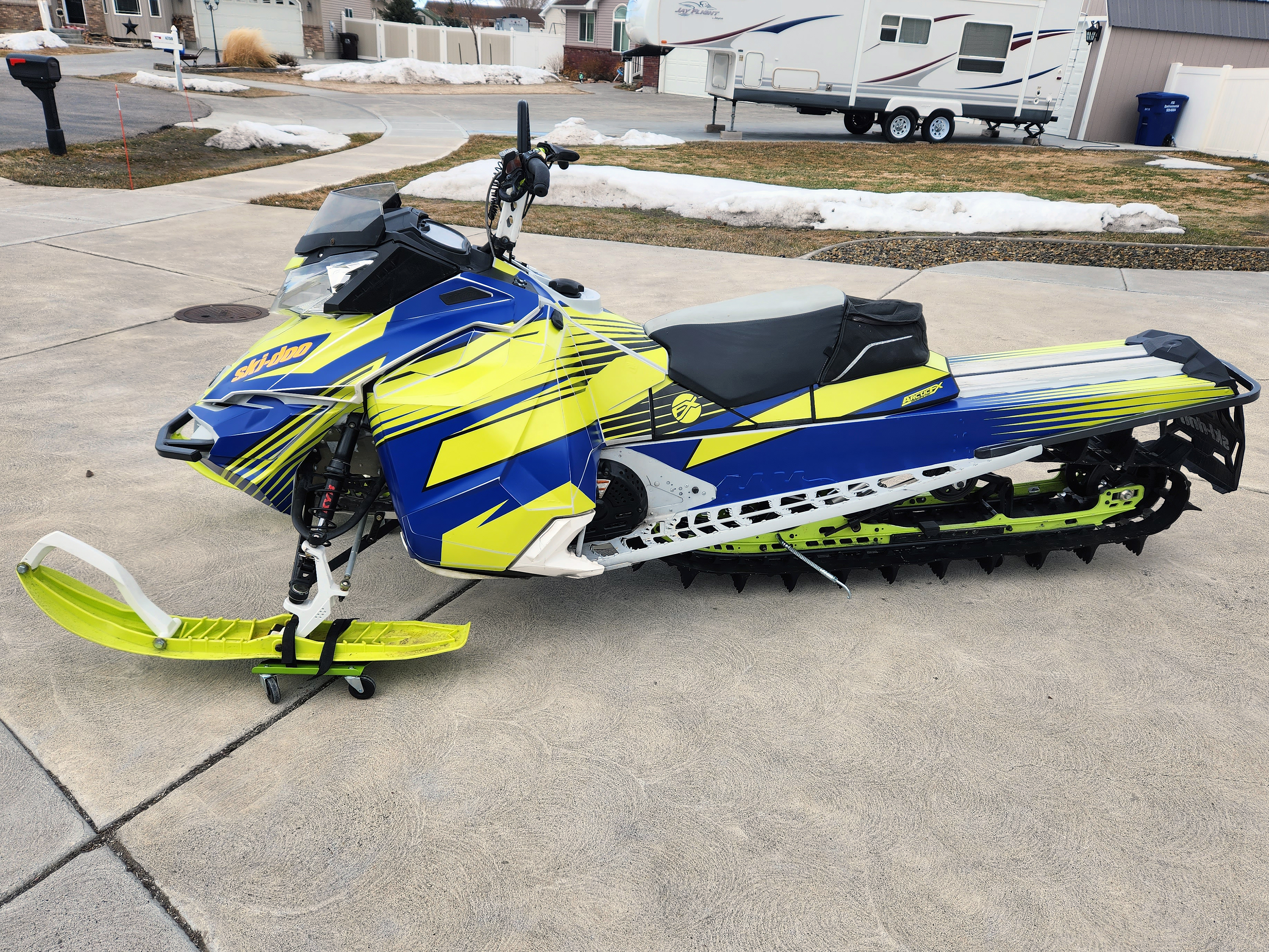A Ski-Doo Rev XM snowmobile with a lime squeeze, blue, and black Justin Thomas Vanquish custom vinyl wrap.
