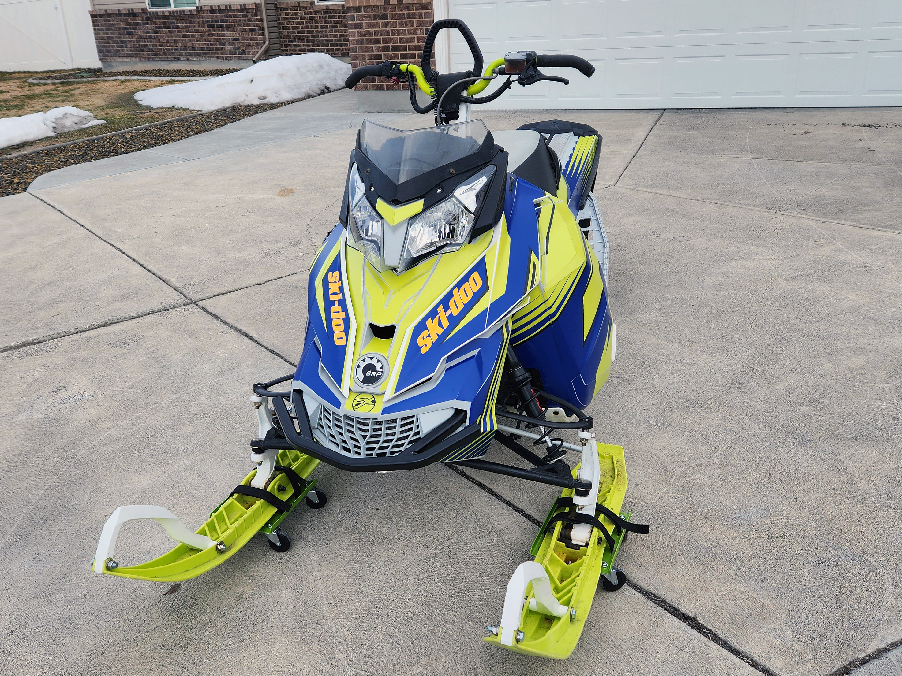 A Ski-Doo Rev XM snowmobile with a lime squeeze, blue, and black Justin Thomas Vanquish custom vinyl wrap.