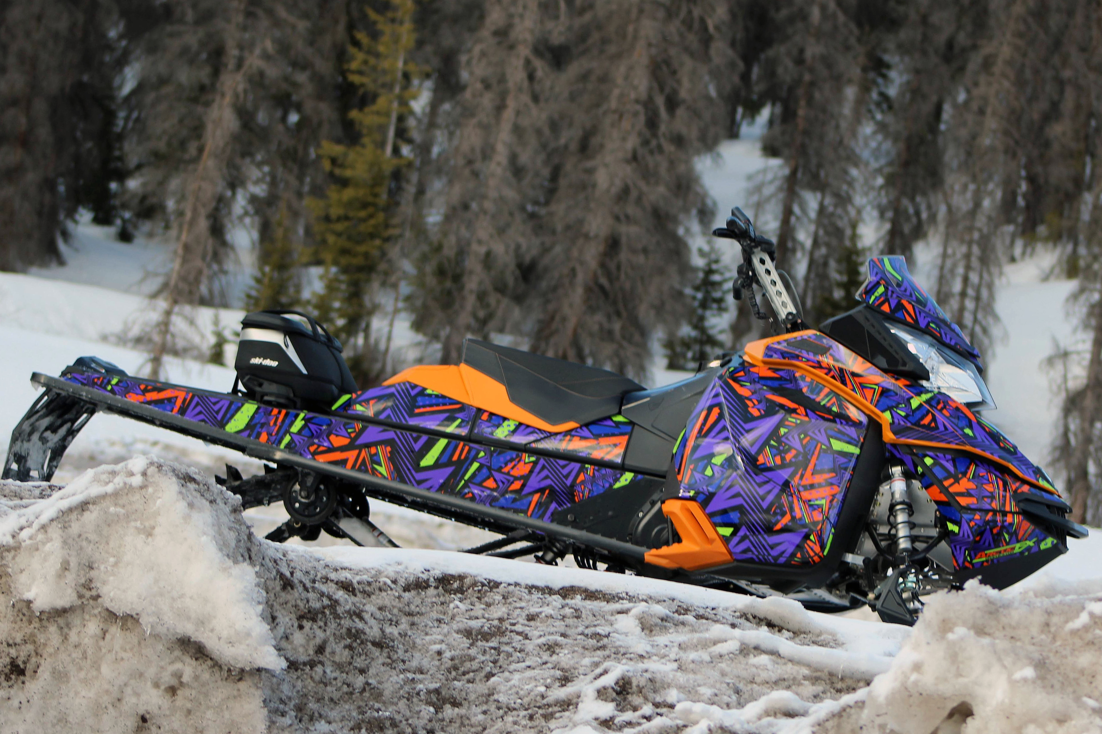A Ski-Doo Rev XM snowmobile with a manta, purple, orange, and black Twisted custom vinyl wrap.
