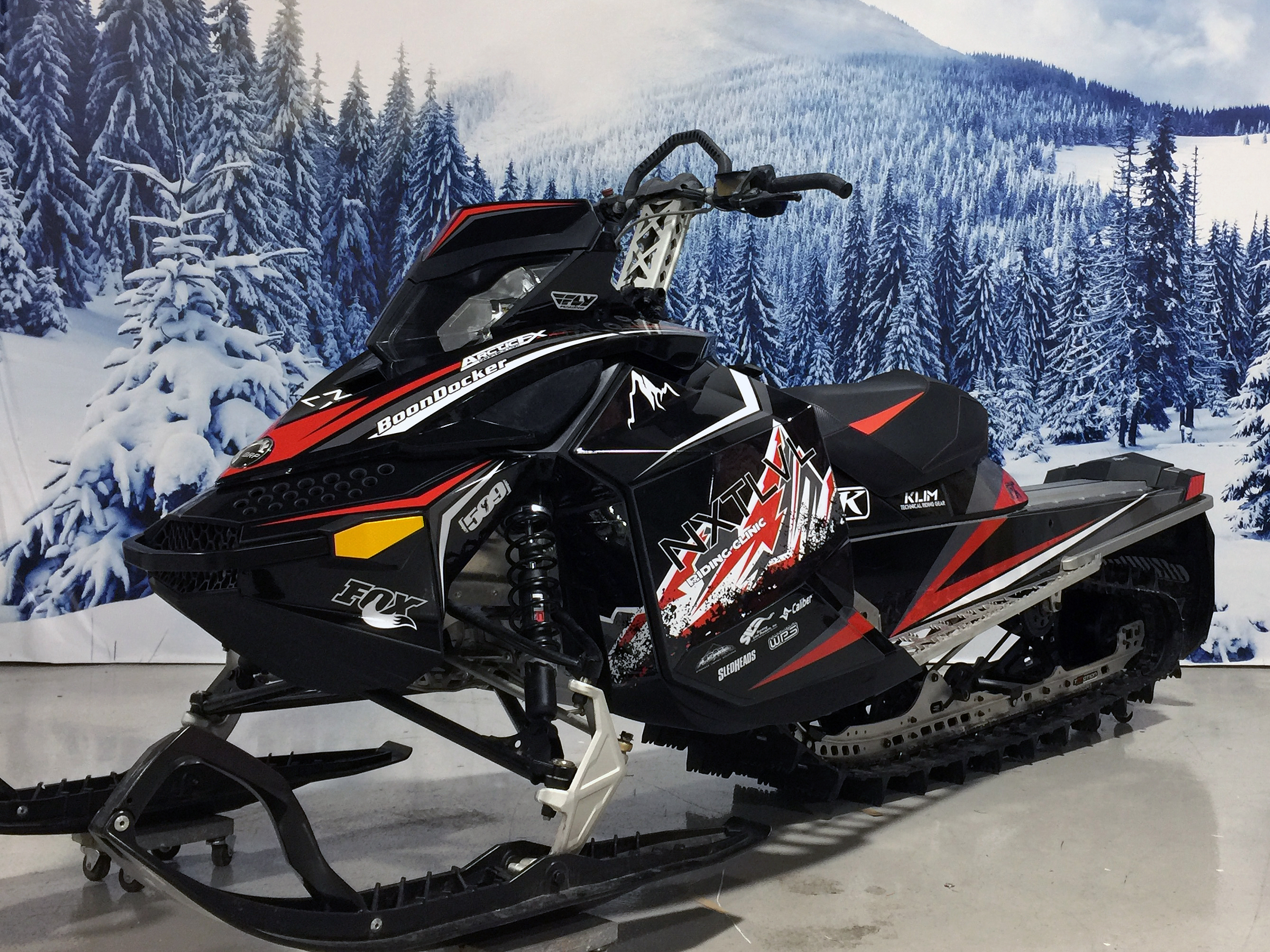 A Ski-Doo Rev XP snowmobile with a black, red, and white Adams Signature custom vinyl wrap.