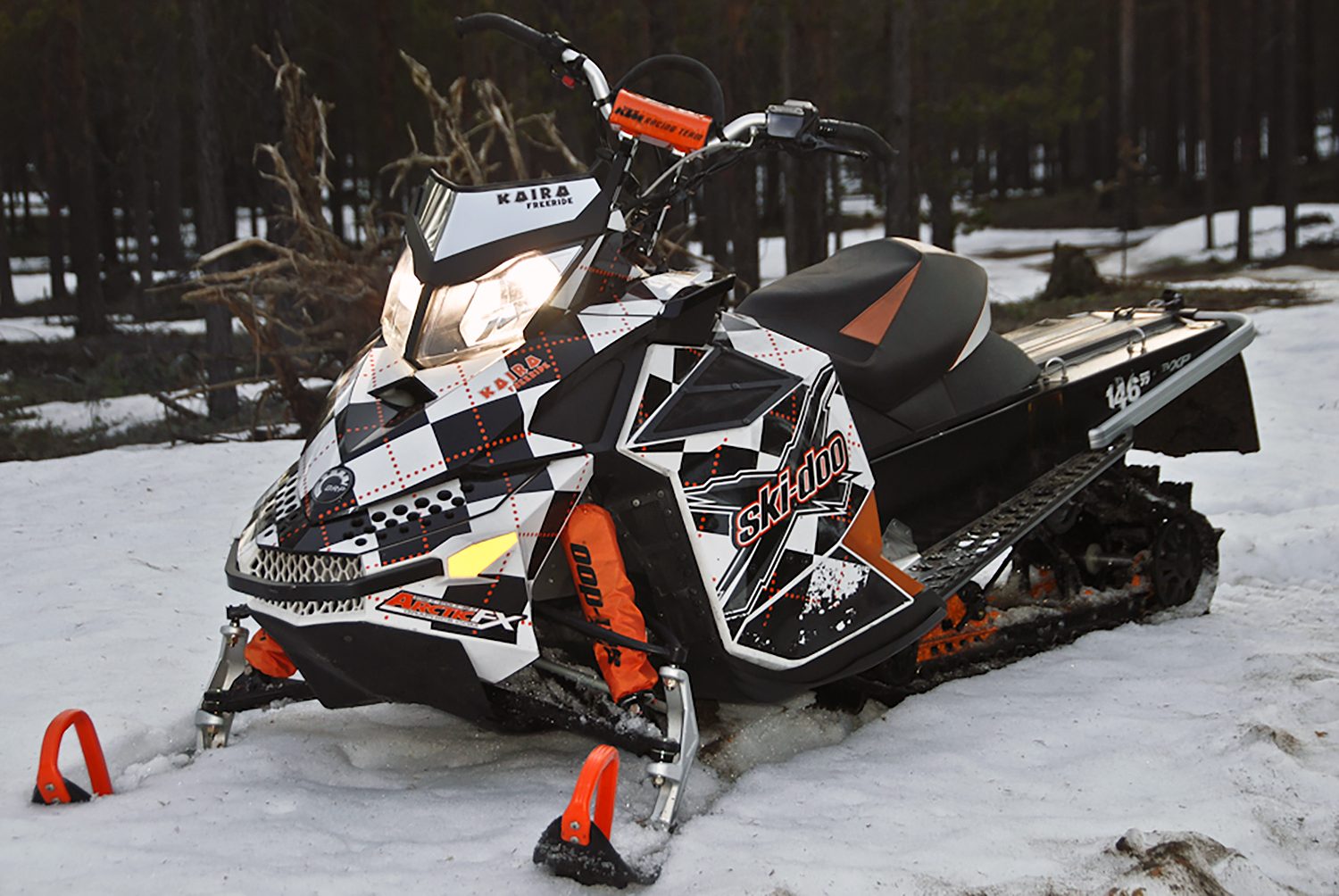 A Ski-Doo Rev XP snowmobile with a black, orange, and white Argyle pattern custom vinyl wrap.