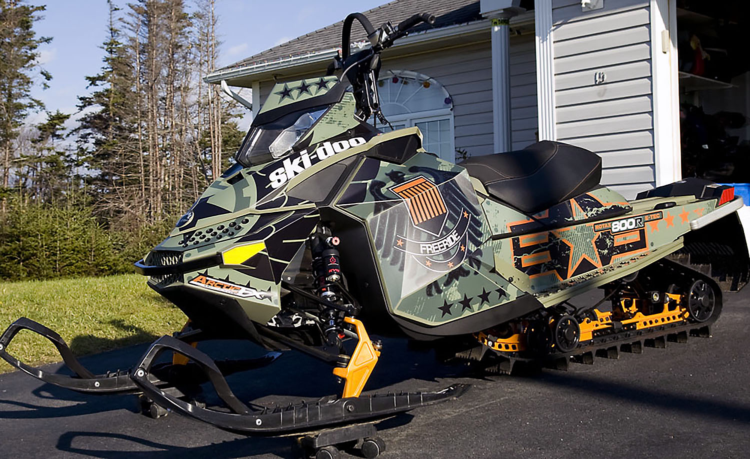 A Ski-Doo Rev XP snowmobile with a army green, black, and orange Freeride custom vinyl wrap.