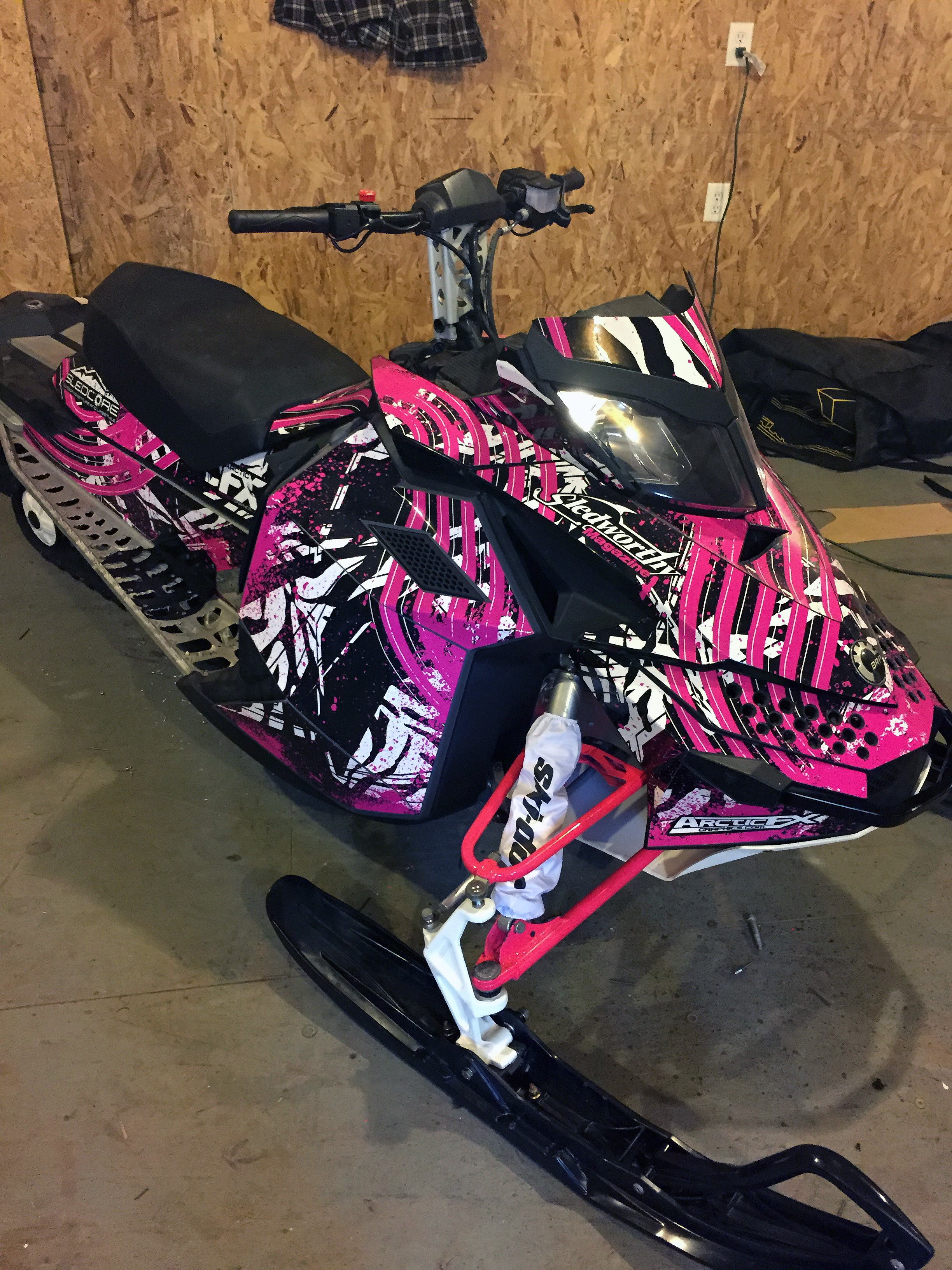 A Ski-Doo Rev XP snowmobile with a black, white, and pink Carnivore custom vinyl wrap.