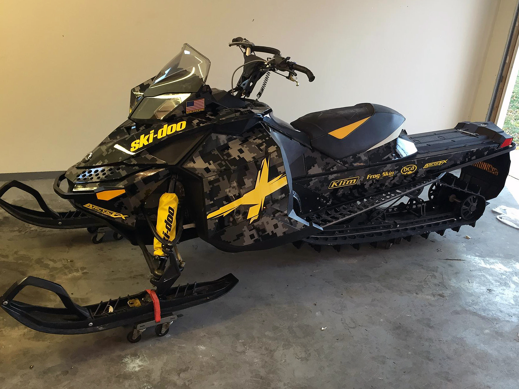 A Ski-Doo Rev XP snowmobile with a black, gray, and yellow Digital Camo custom vinyl wrap.
