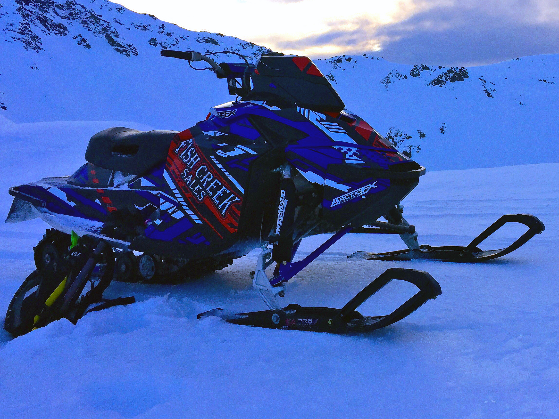 A Ski-Doo Rev XP snowmobile with a blue, white, red, and black stripes Evasion custom vinyl wrap.