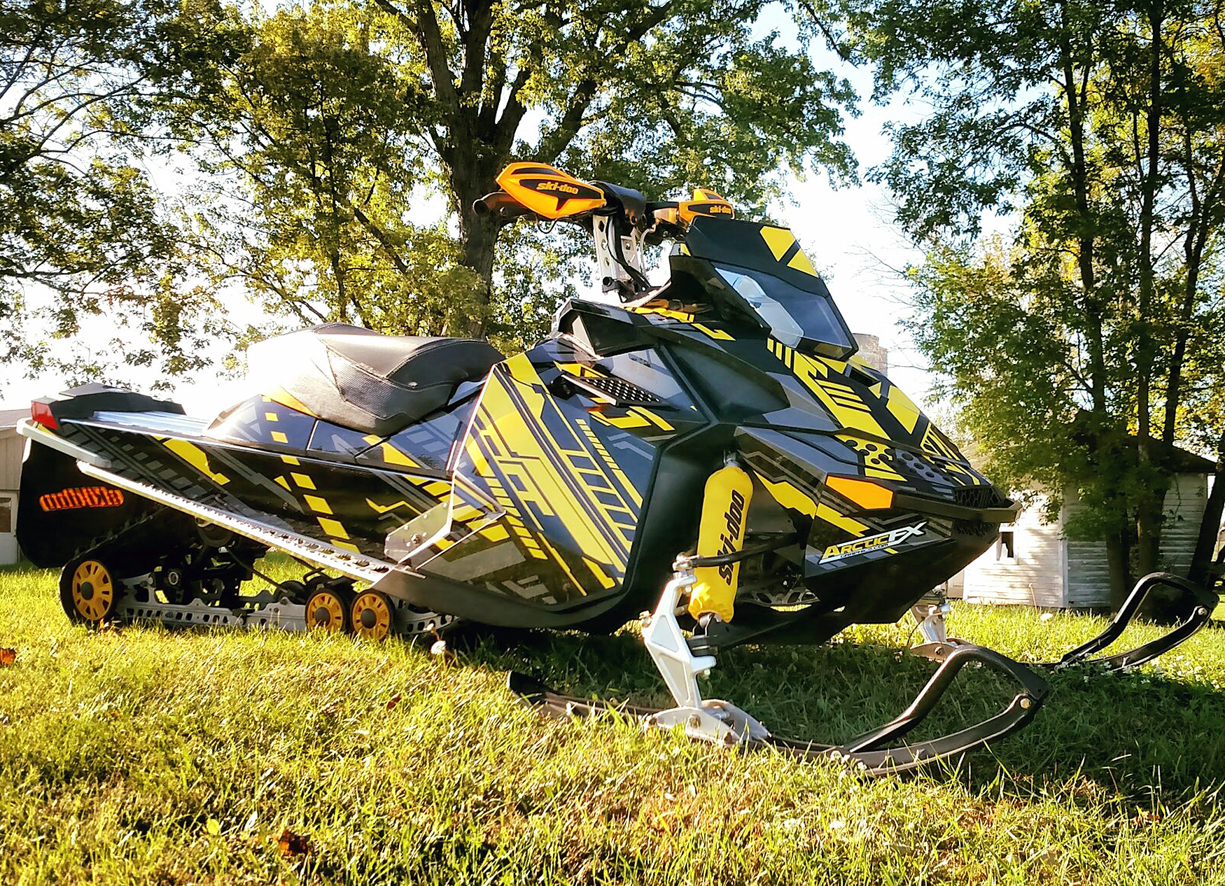 A Ski-Doo Rev XP snowmobile with a yellow, gray, and black stripes Evasion custom vinyl wrap.