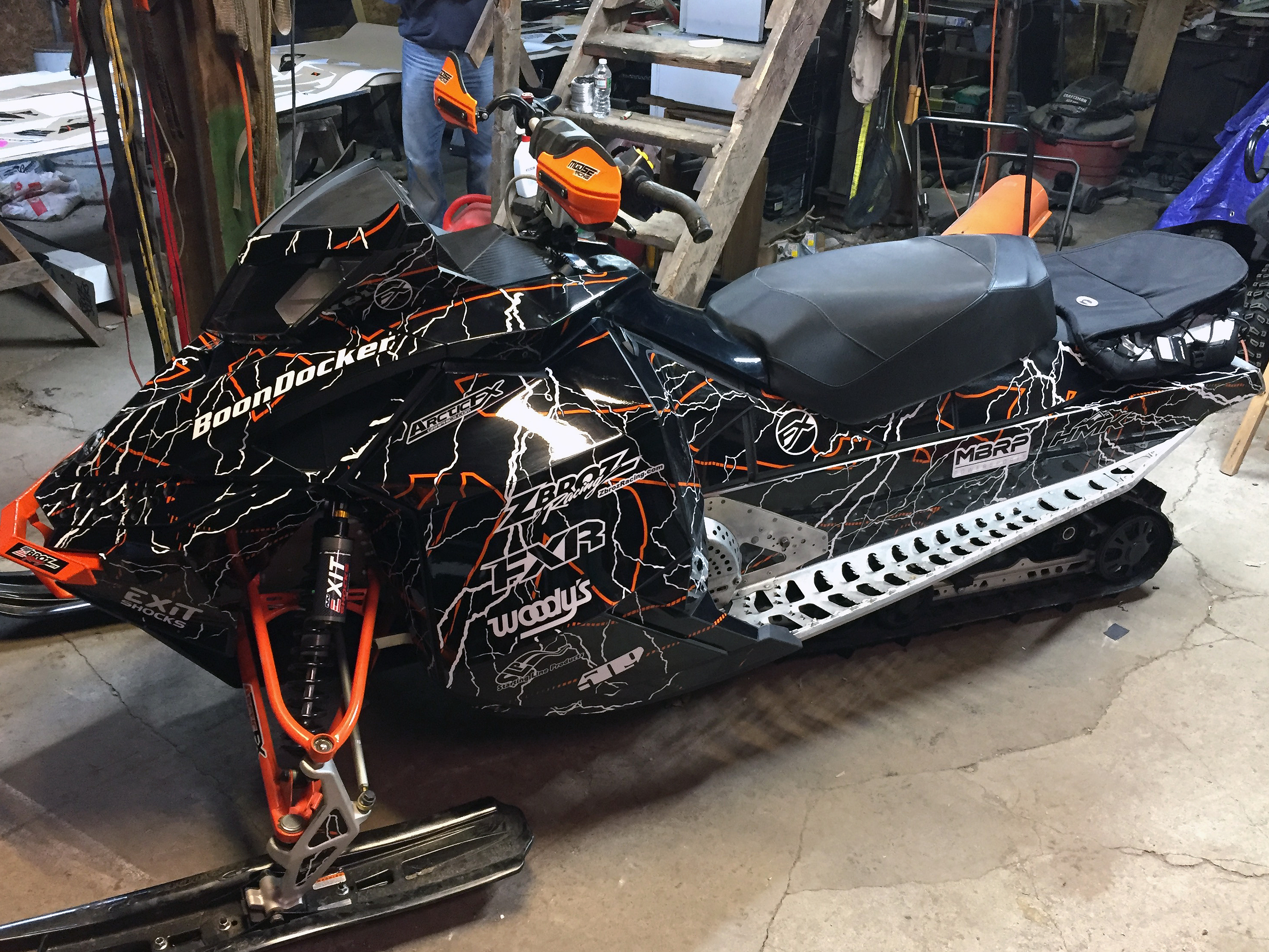 A Ski-Doo Rev XP snowmobile with a orange, white, and black lightning Hard Rain custom vinyl wrap.