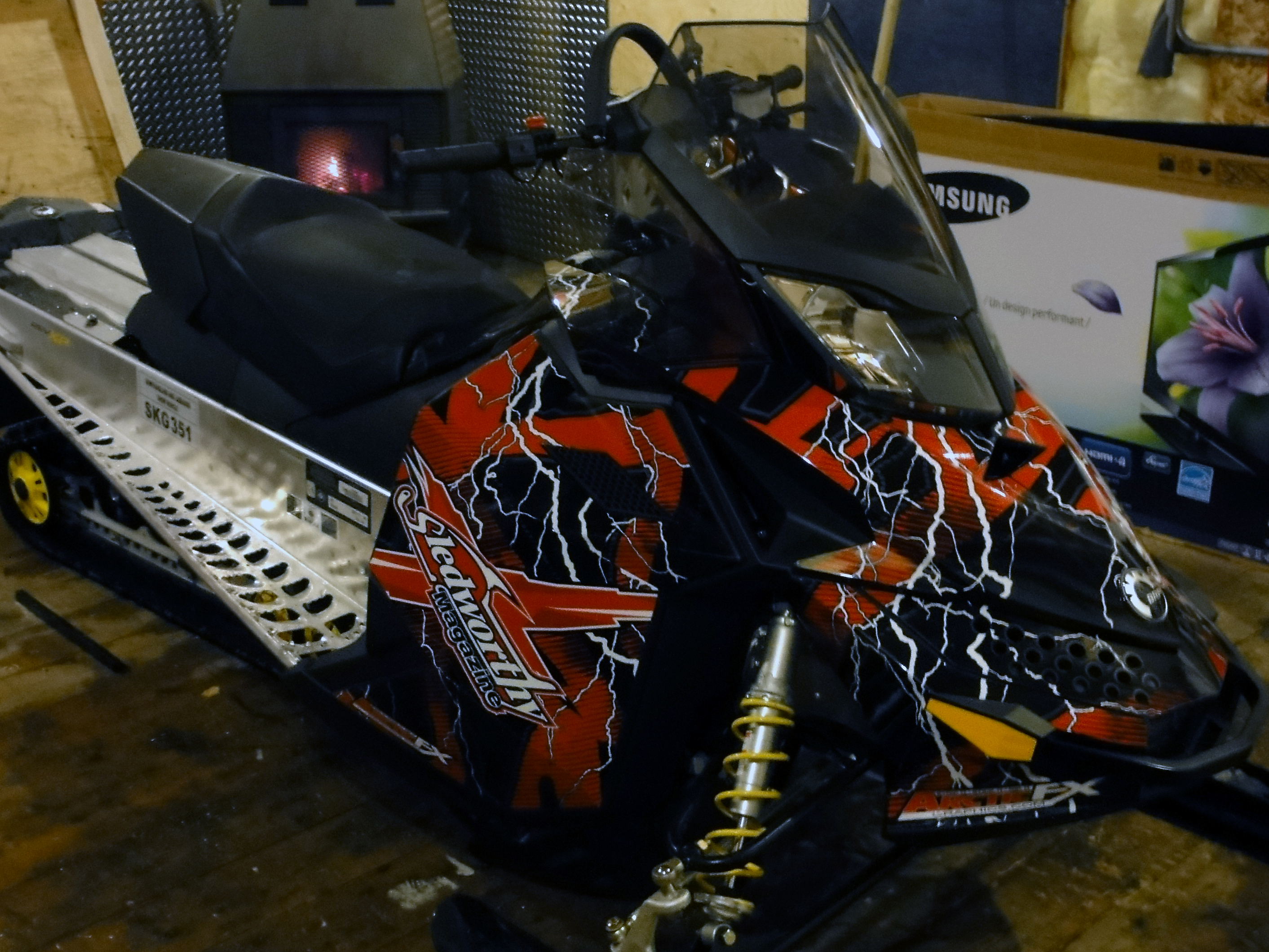 A Ski-Doo Rev XP snowmobile with a red, white, and black lightning Hard Rain custom vinyl wrap.