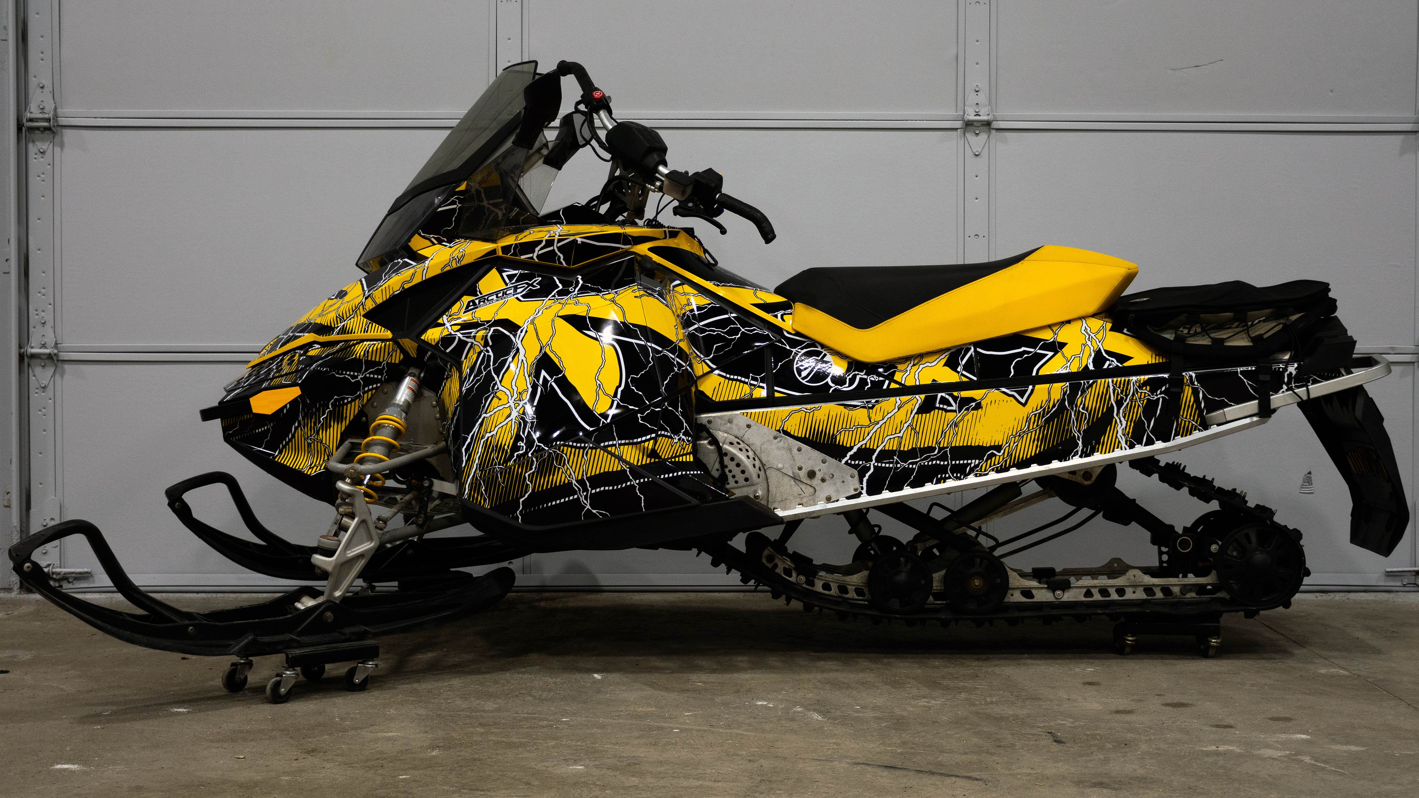 A Ski-Doo Rev XP snowmobile with a yellow, white, and black lightning Hard Rain custom vinyl wrap.