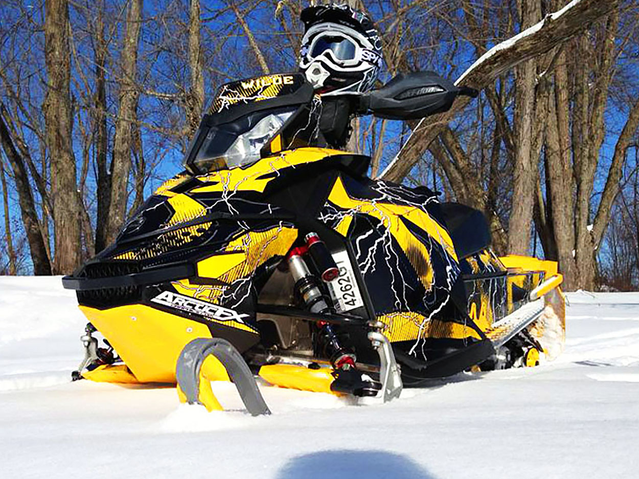 A Ski-Doo Rev XP snowmobile with a yellow, white, and black lightning Hard Rain custom vinyl wrap.