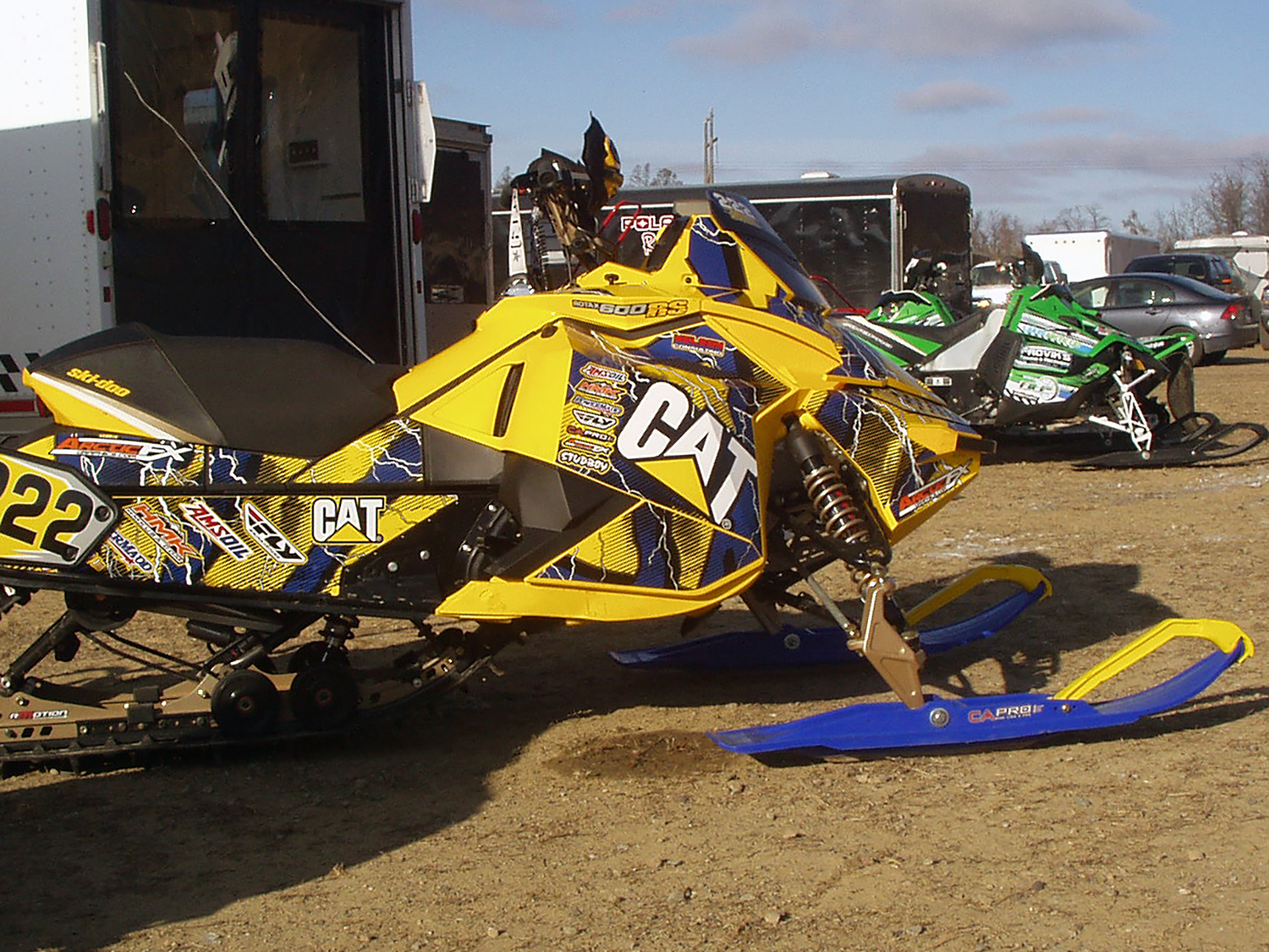 A Ski-Doo Rev XP snowmobile with a yellow, white, and blue lightning Hard Rain custom vinyl wrap.